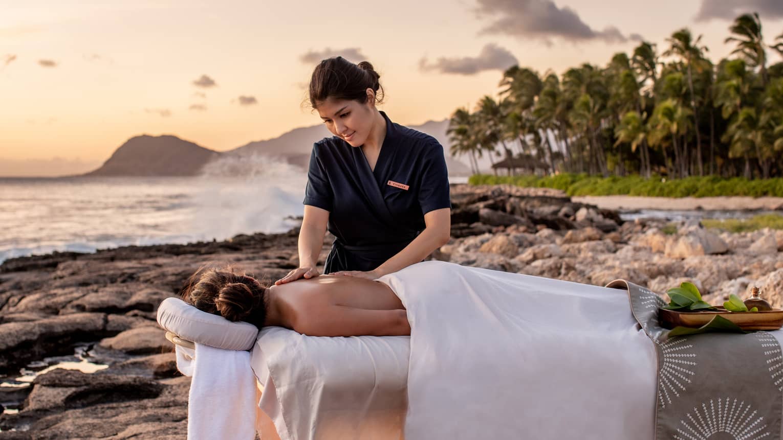 A four seasons guest receives a massage on the beach, as the sun sets in the distance