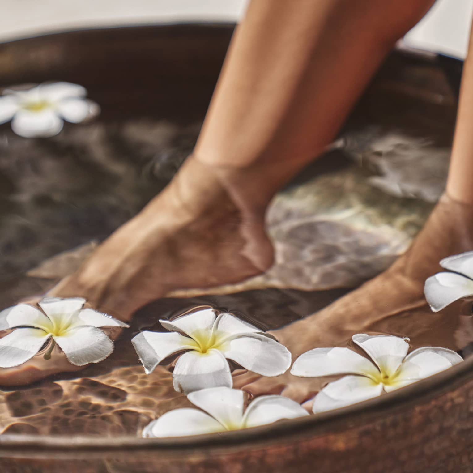 A woman's feet in a bowl of water and flowers.