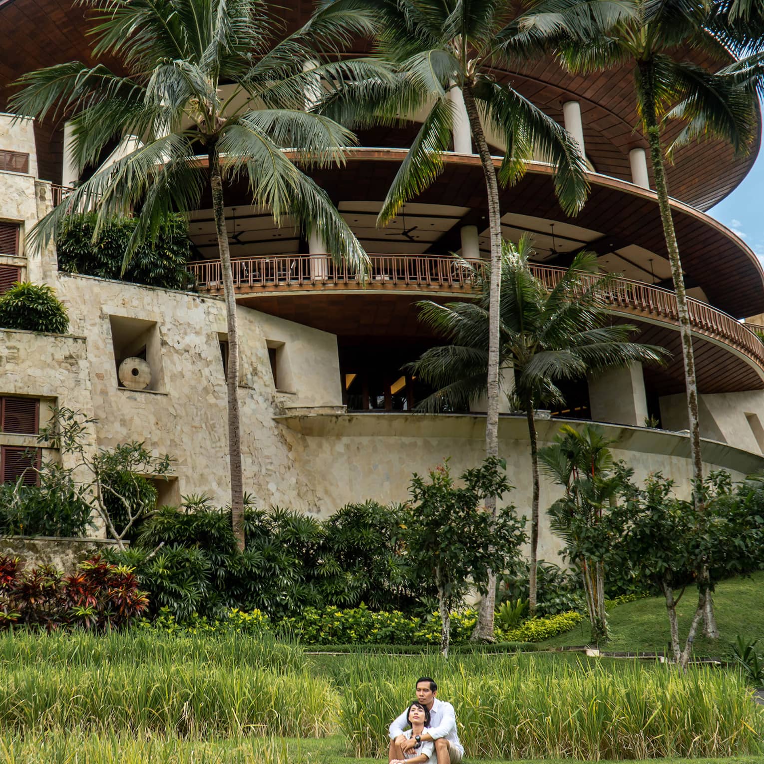 Long view of a couple embracing on the grass in front of the rice-bowl inspired Four Seasons Resort Bali at Sayan.