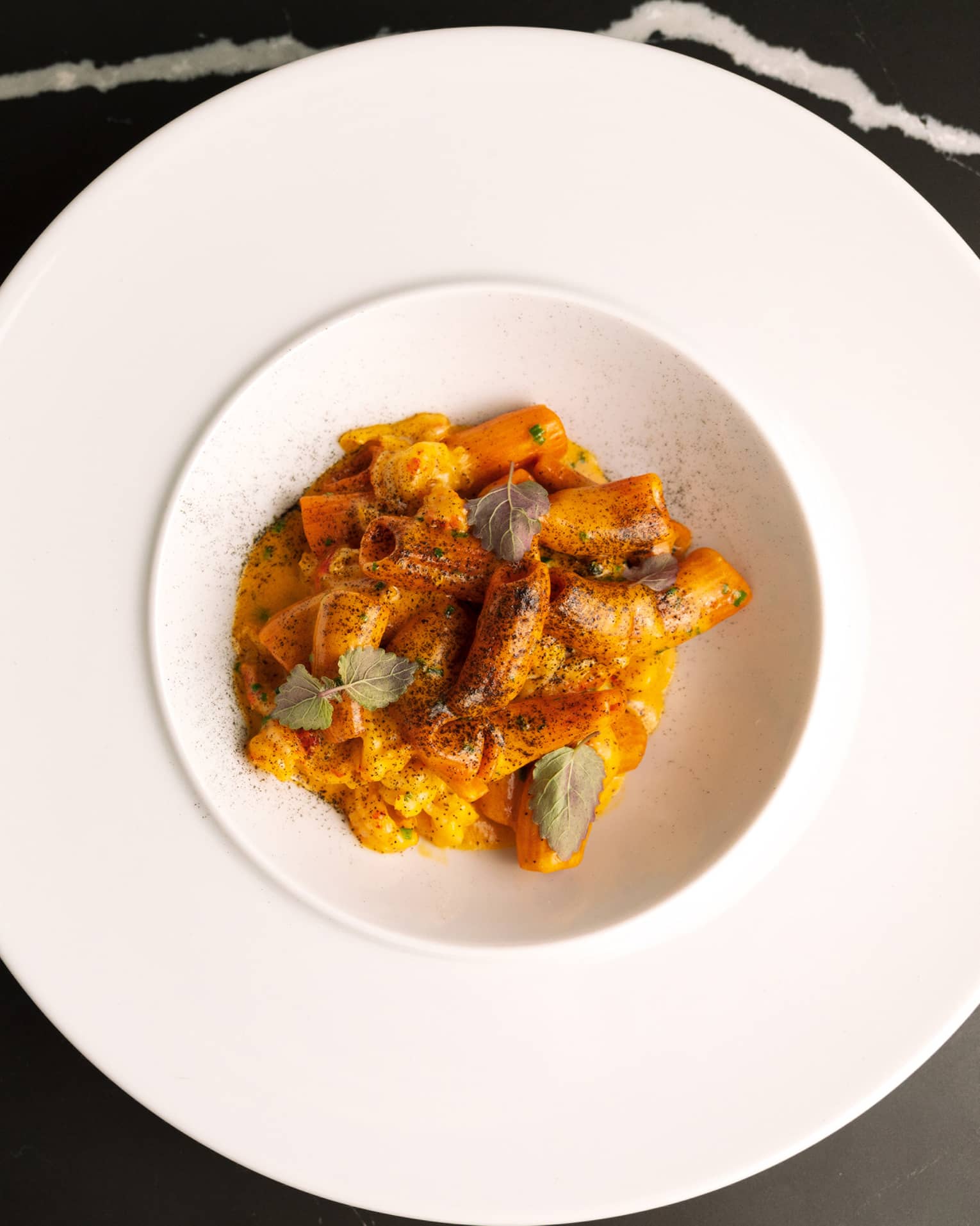 Pasta in a white bowl on a black table.