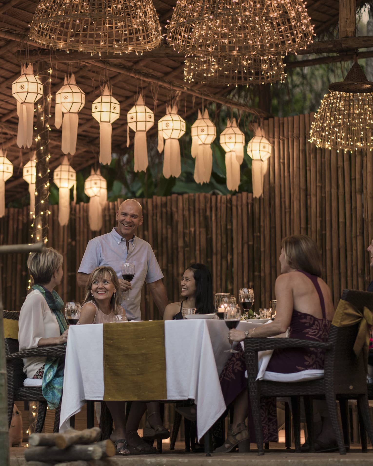 A group of people sitting at a table enjoying a meal in outdoor pavilion decorated with lanterns