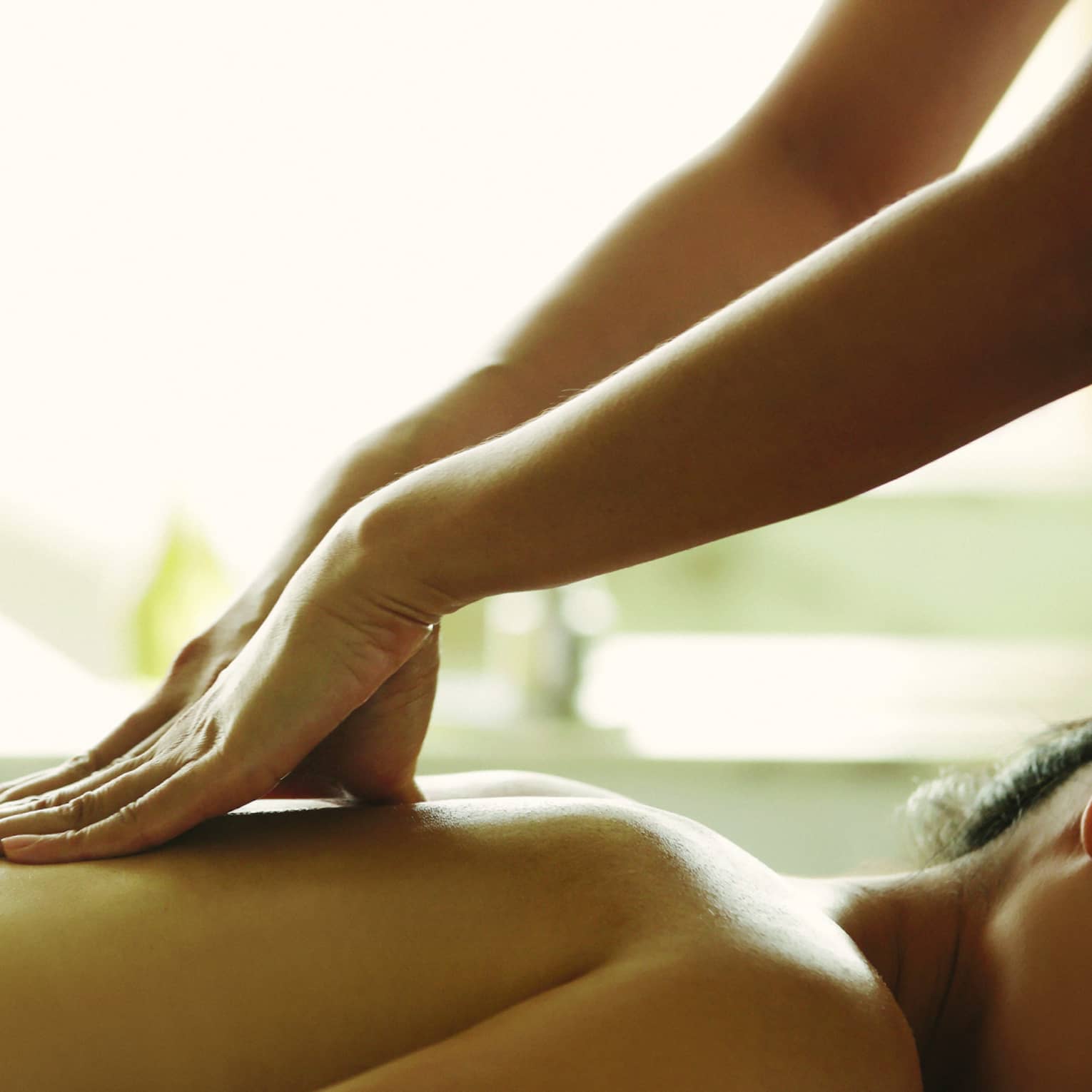 Masseuse reaches over, massages woman's bare back as she lies on spa table