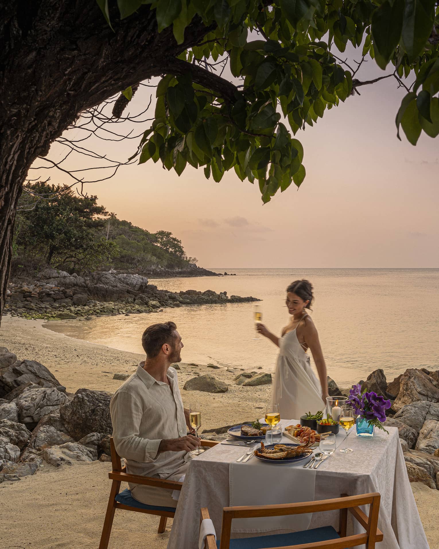 A beach dinner date at dusk, with a couple enjoying a serene seaside view.