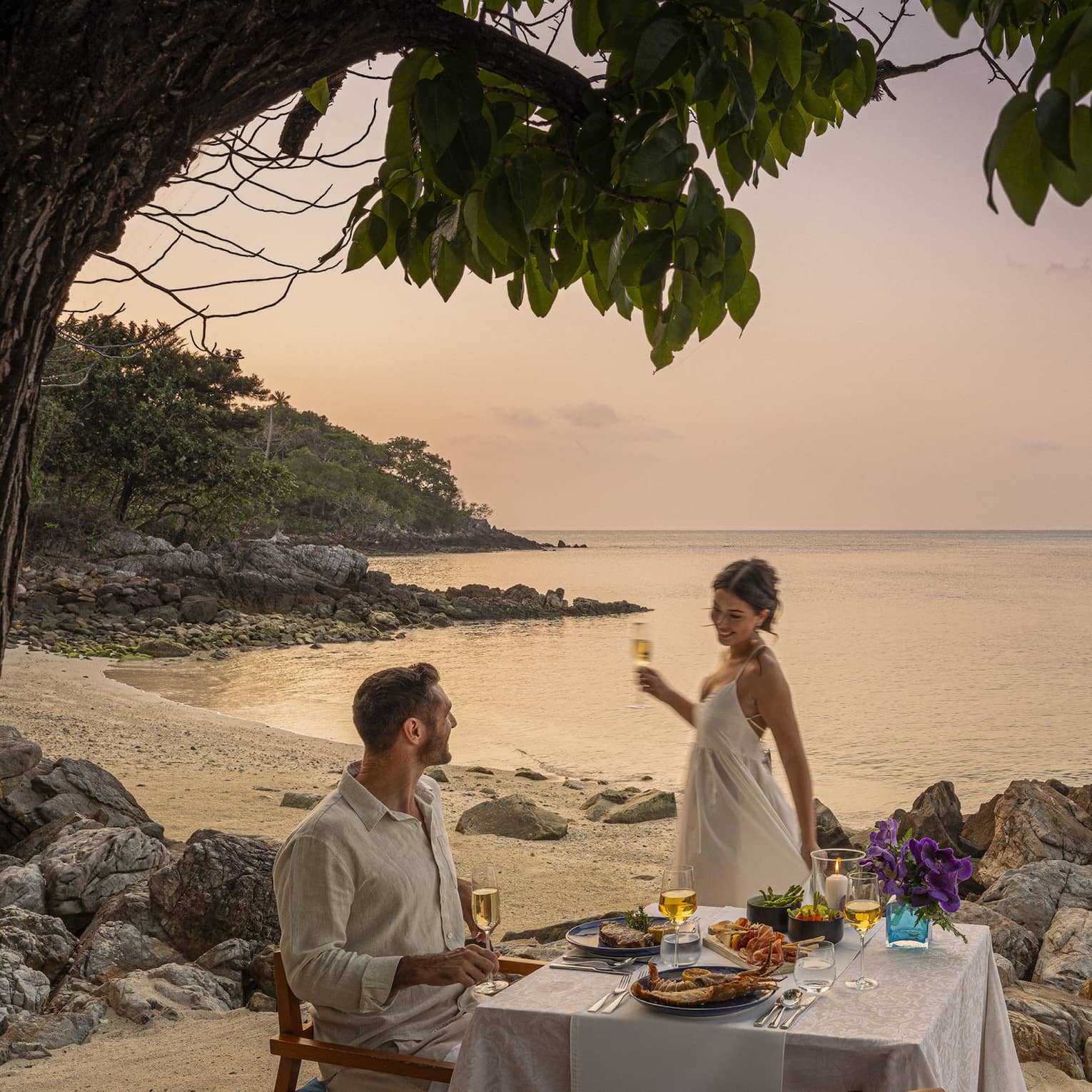 A beach dinner date at dusk, with a couple enjoying a serene seaside view.
