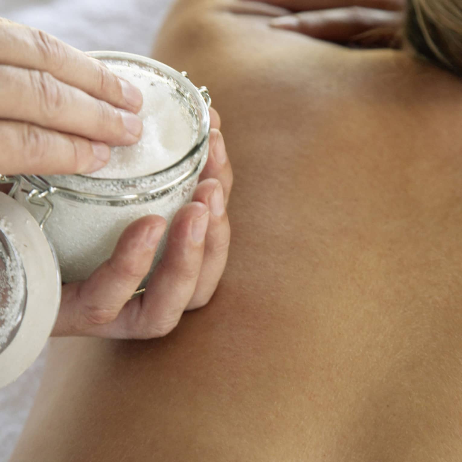 Jar of sea salt scrub above woman's bare back in spa
