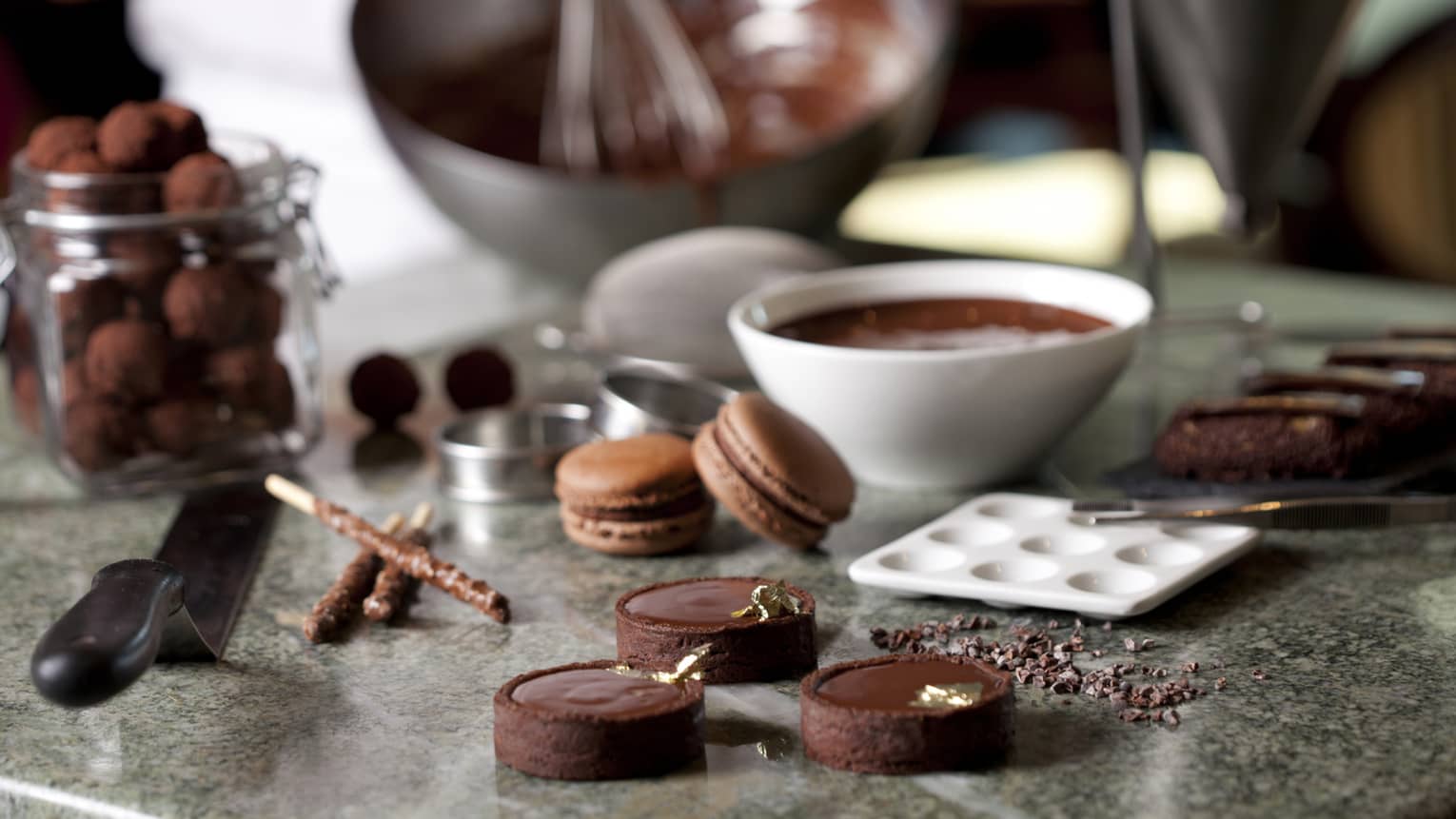 Close-up of fine chocolates, macarons, bowl of melted chocolate on counter