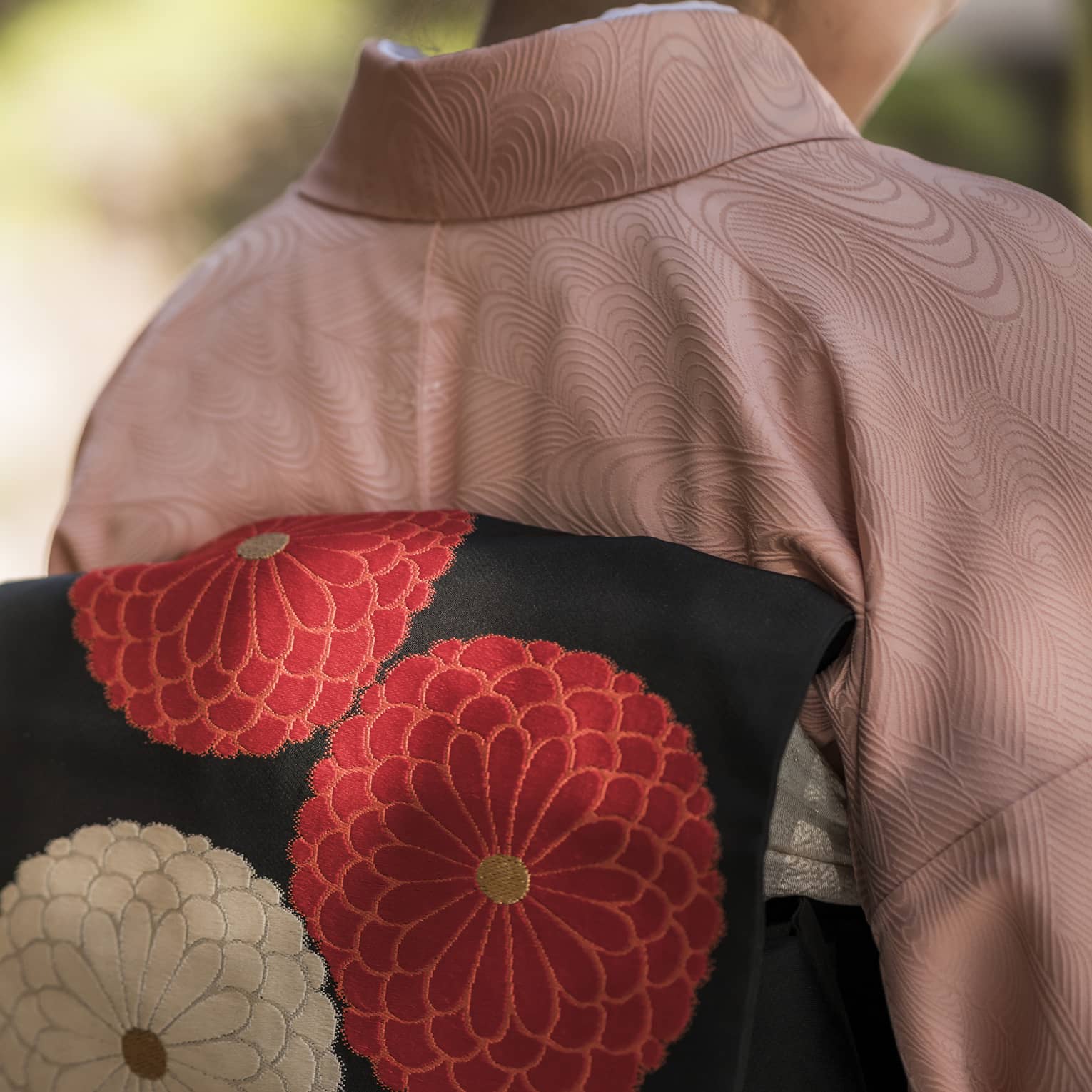 Back view of a person wearing a pink kimono with a black obi featuring red and white floral designs