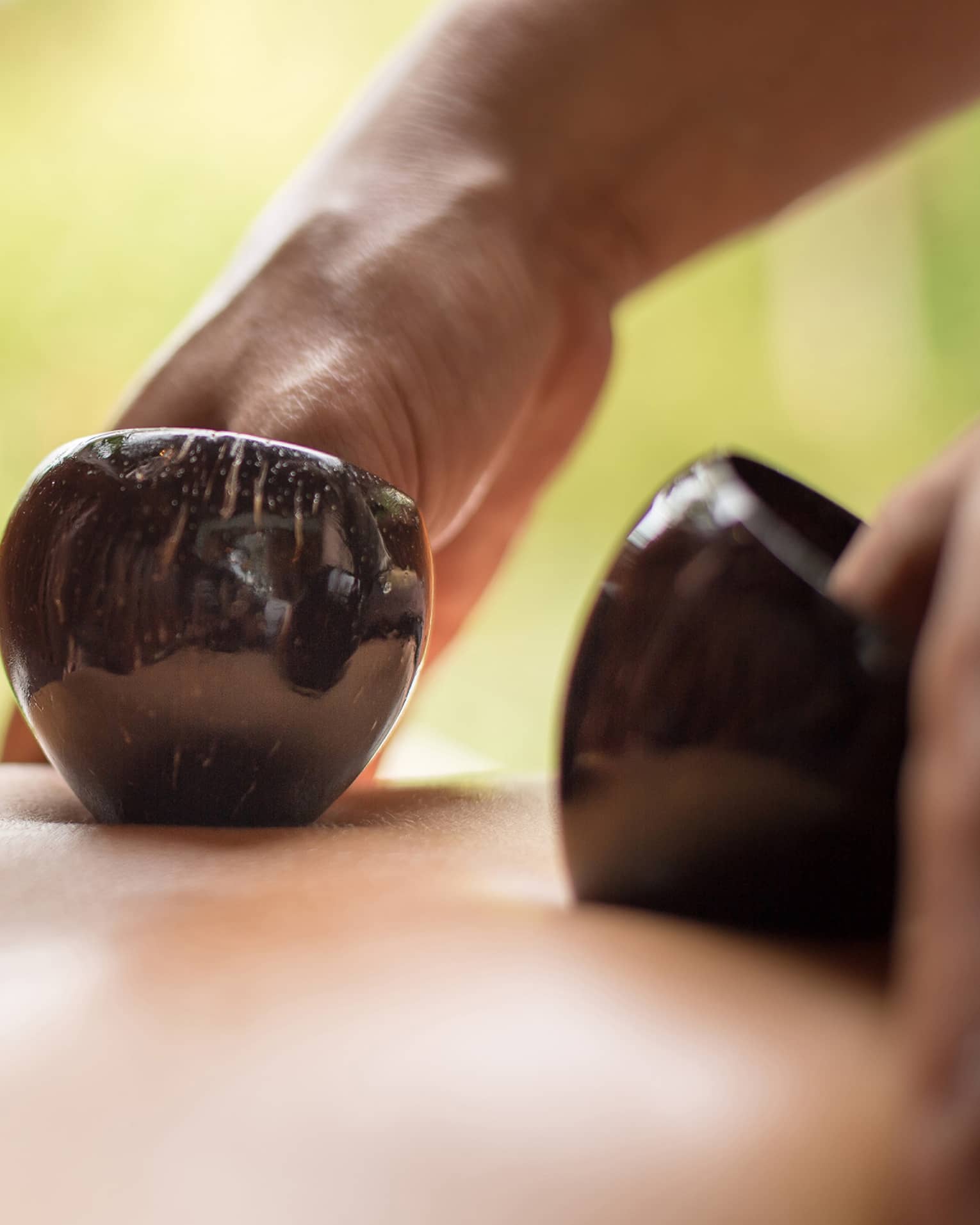 Close-up of hands massaging bare back with black coconut shells