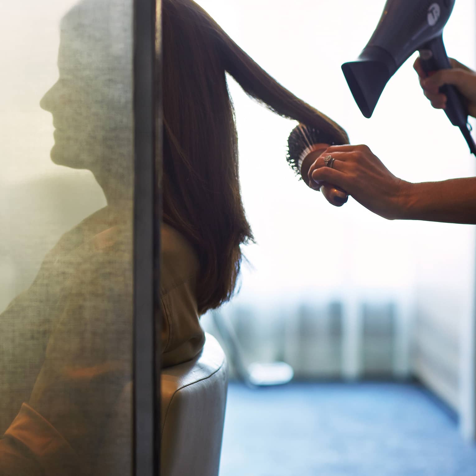 Silhouette of woman behind salon screen as hairdressers brushes, blow dries hair