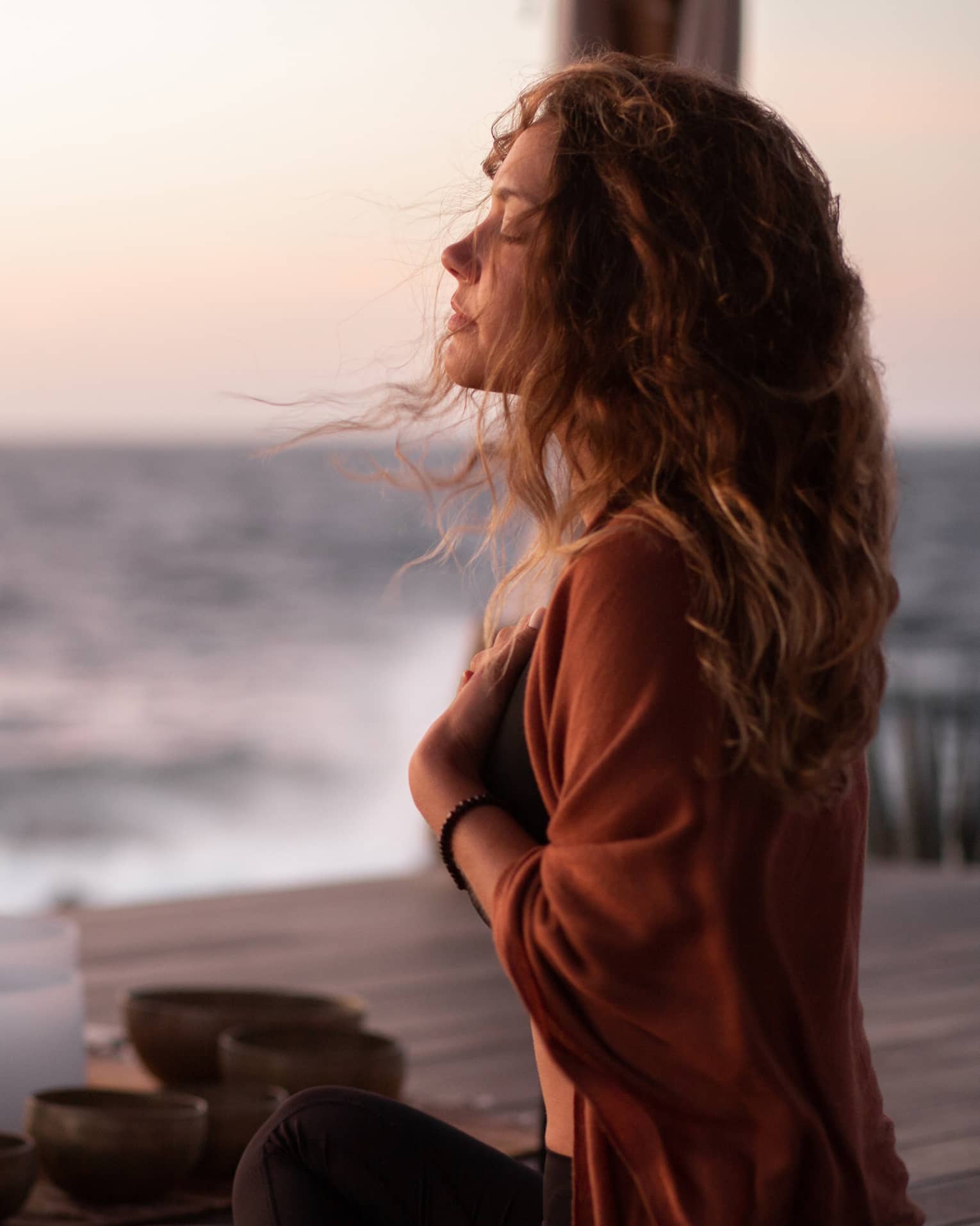 A woman participating in breathwork and sound meditation outside near an ocean.