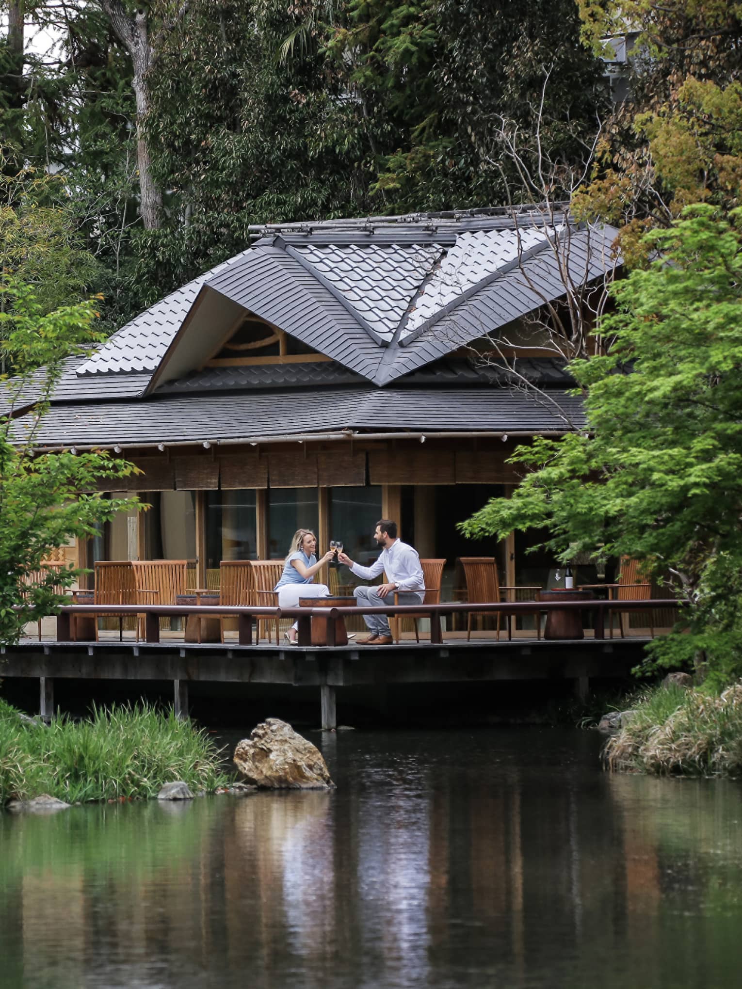 View across pond to restaurant patio where couple toasts with wine glasses