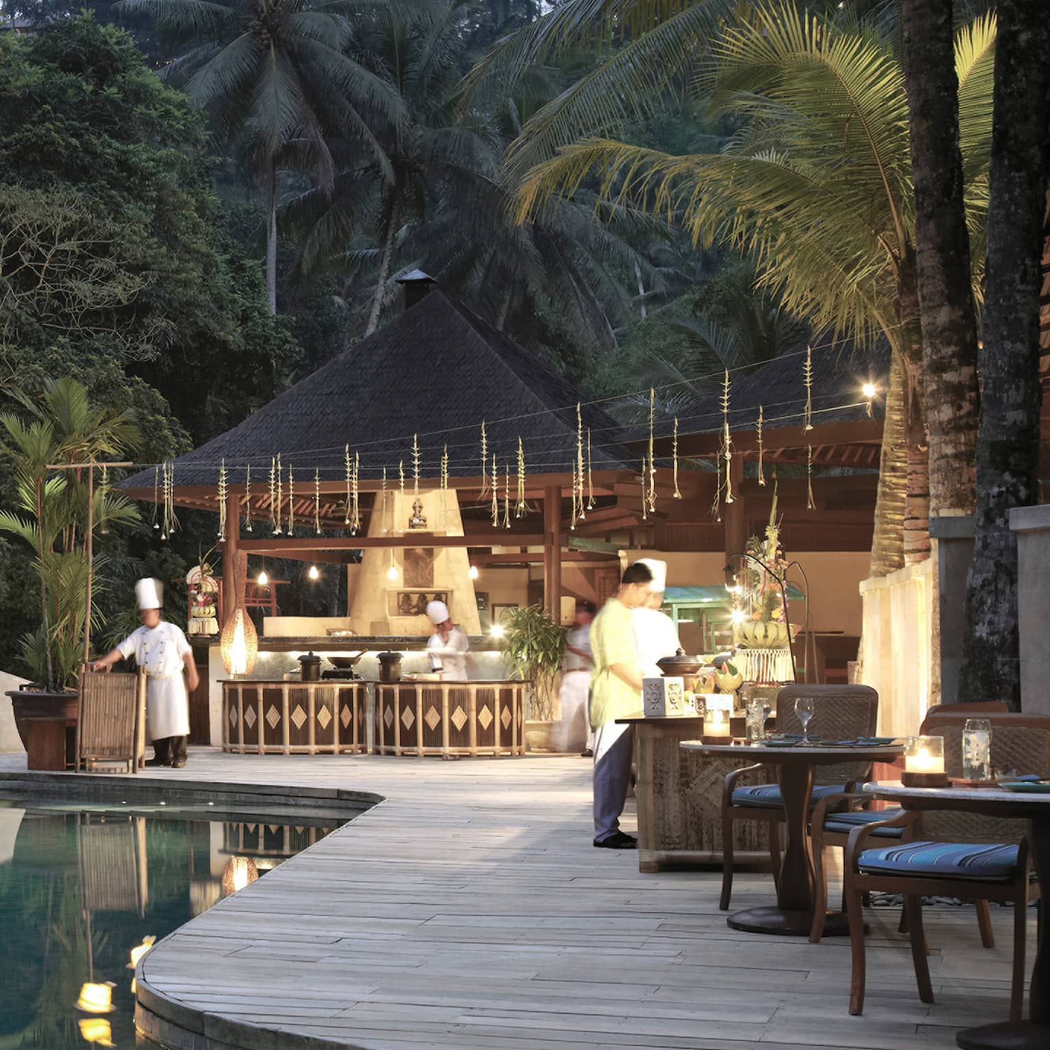 An infinity pool looking out towards the dense jungle; chefs bustle around the outdoor kitchen on the poolside deck.