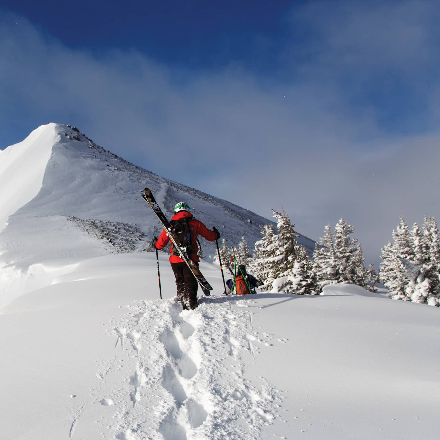 Two people with skis on their backs walking in snow.