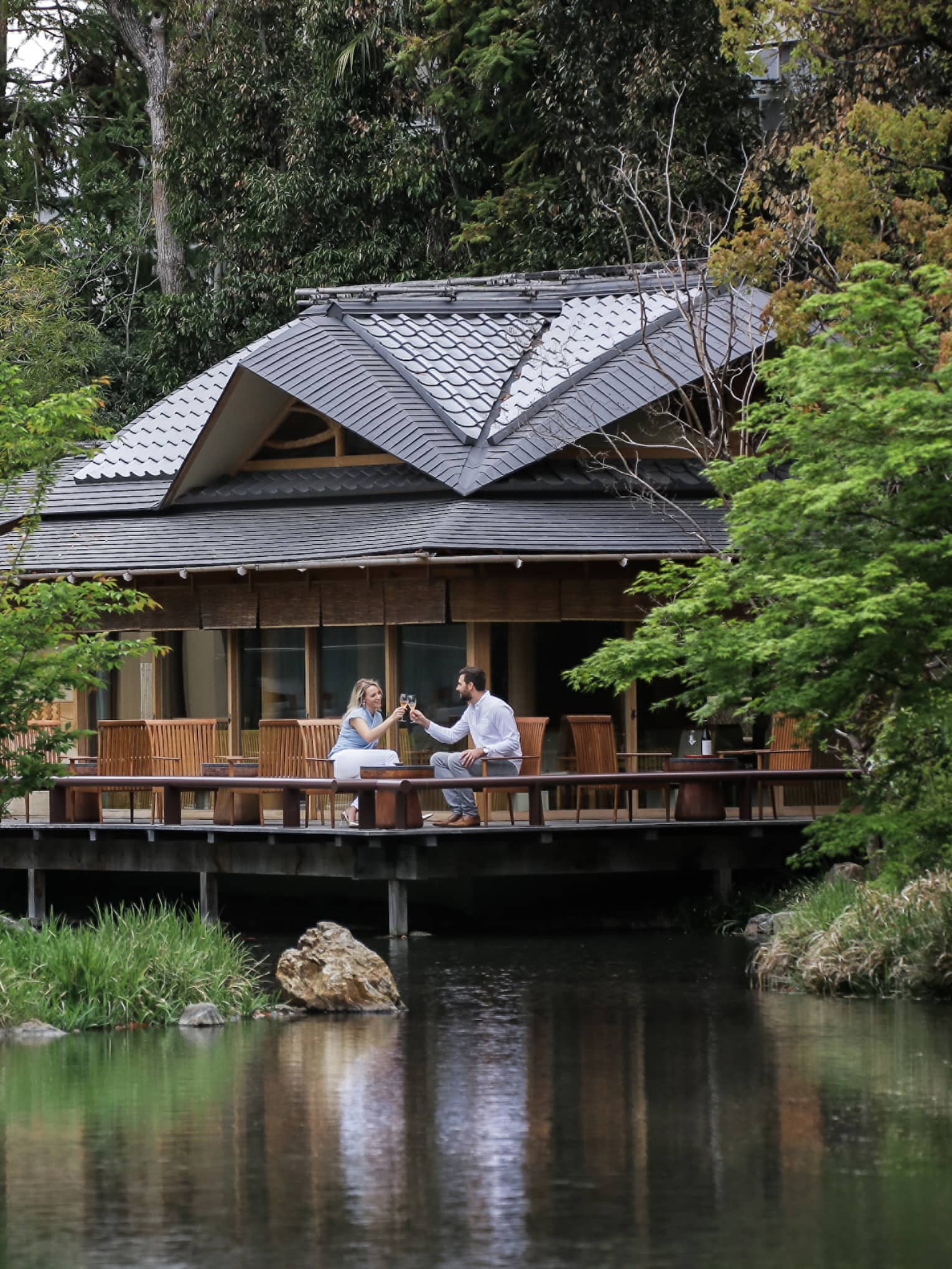 View across pond to restaurant patio where couple toasts with wine glasses