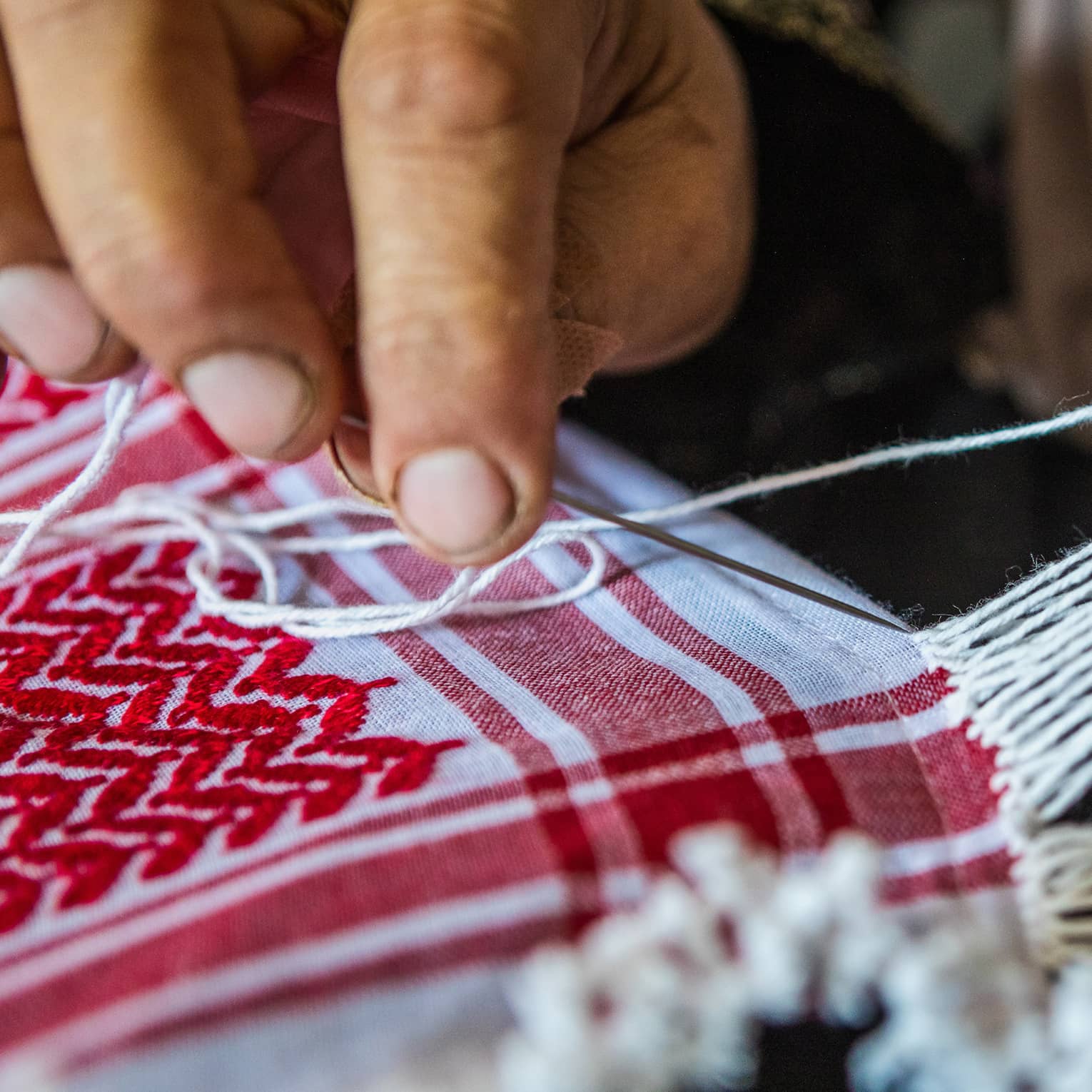 A person weaving strands of fabric together to create a quilt.