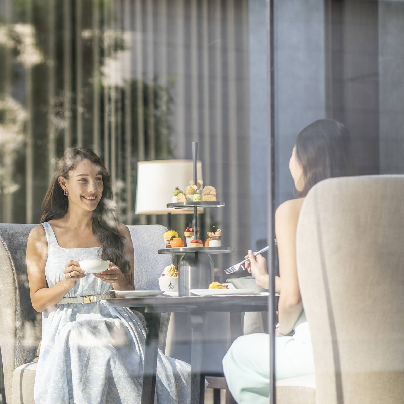 View through cafe glass window where two women enjoy afternoon tea and desserts