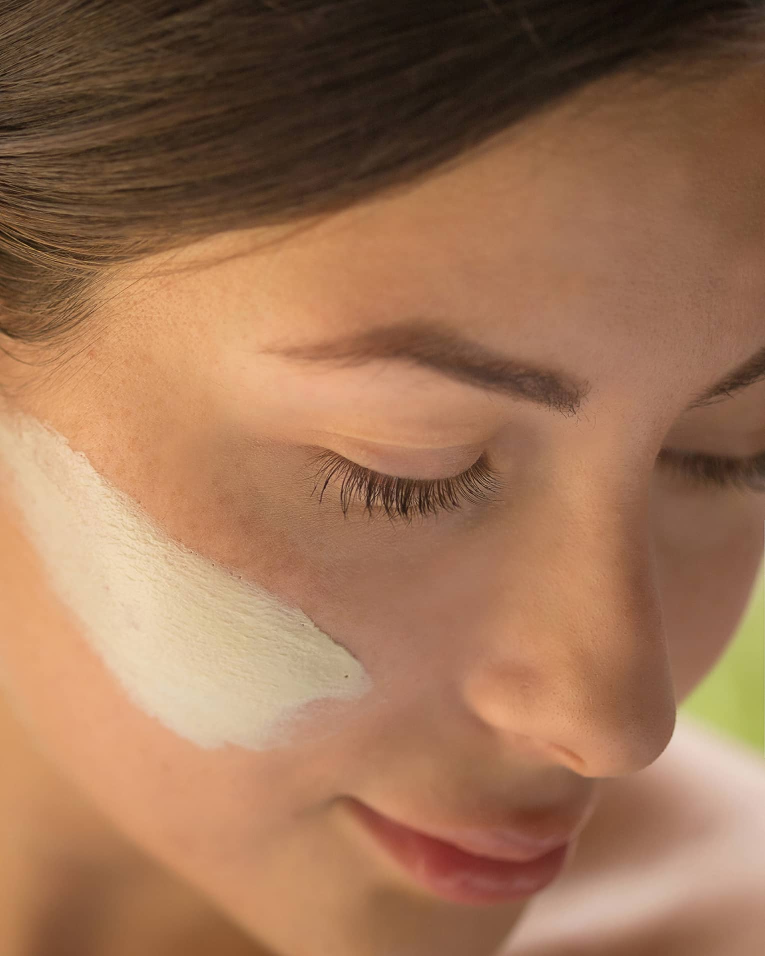 Close-up of side of woman's face with lotion on cheek