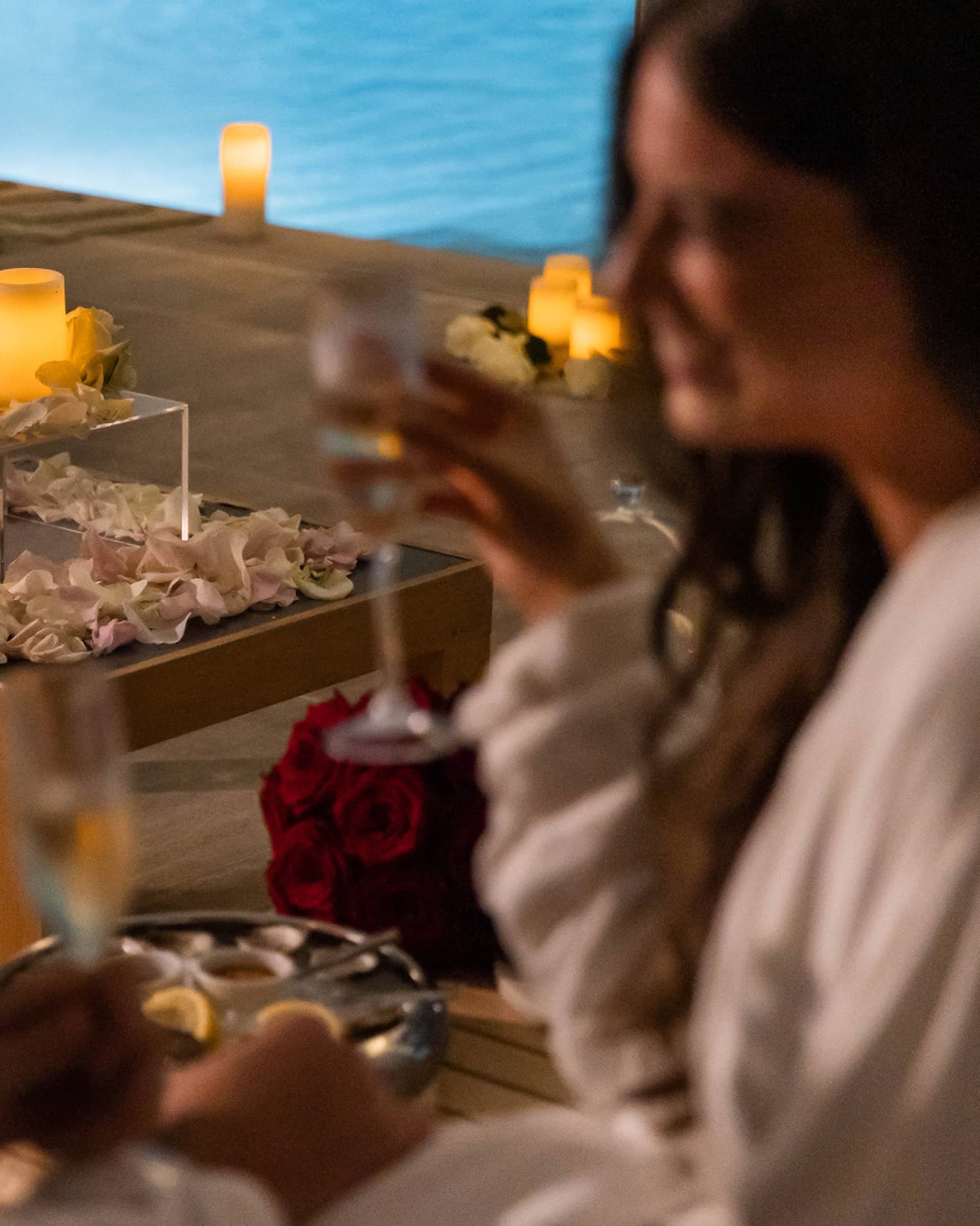 A couple with wine in hand near a pool surrounded by flowers petals and candles.