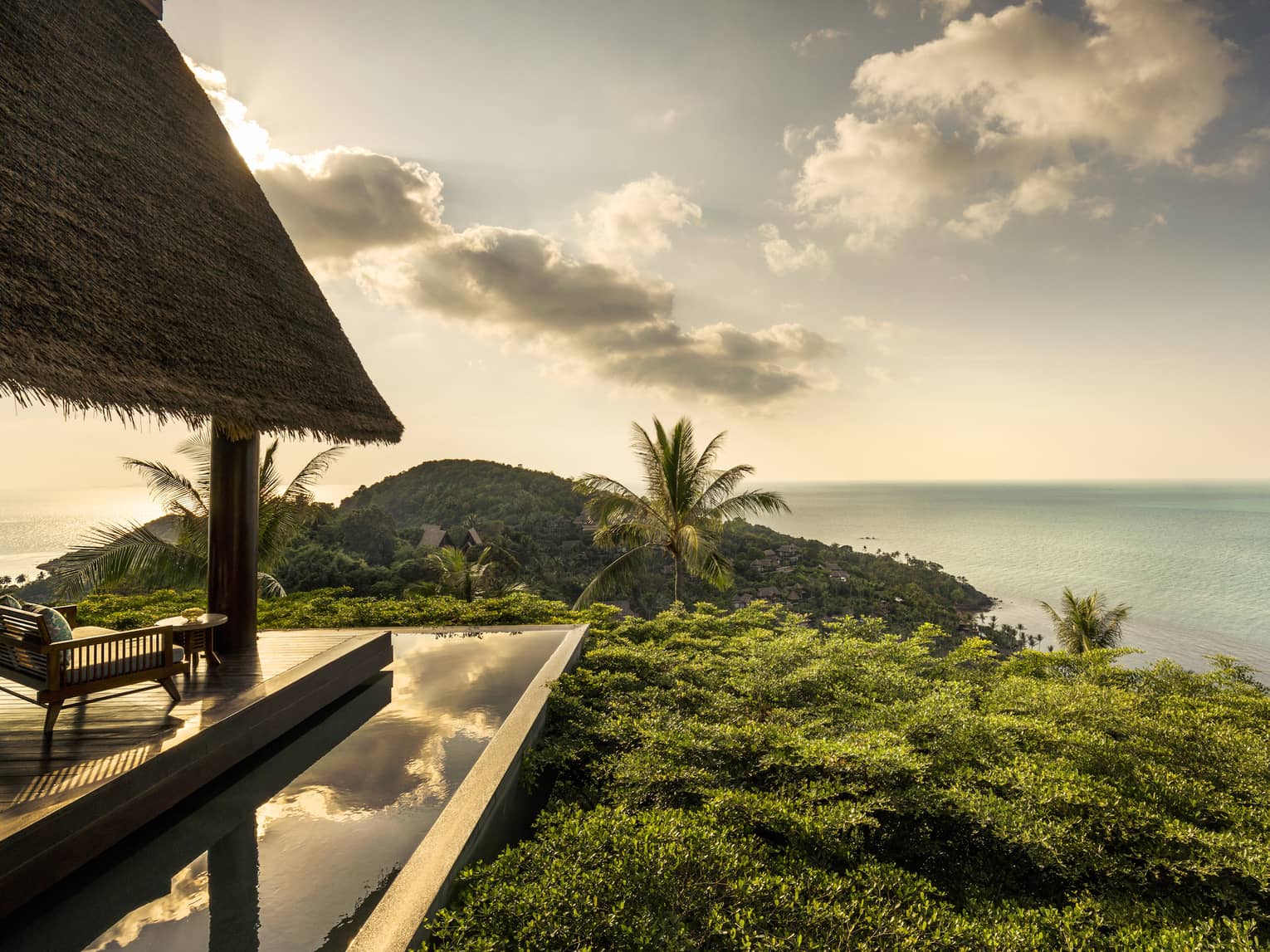 Patio lounge chair, thatched roof and deck overlooking canopy of tropical trees, ocean