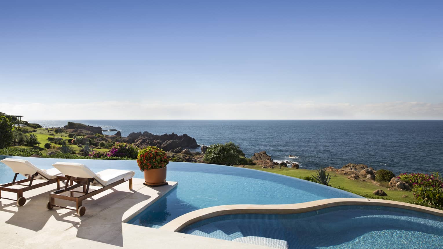 Terrace with two lounge chairs and large infinity pool, overlooking the sea