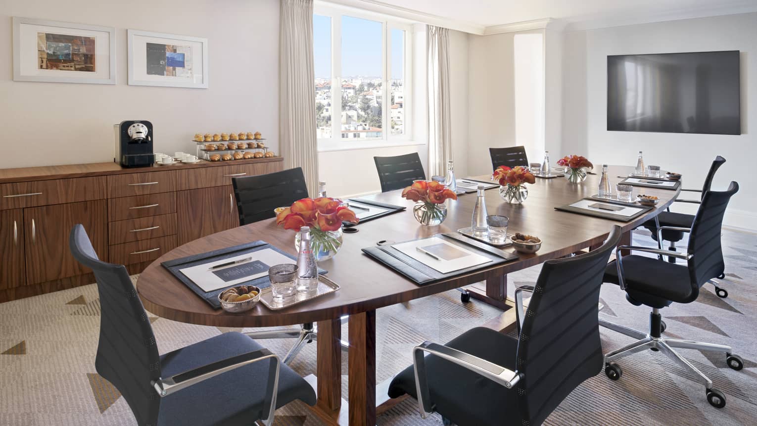 A circular mahogany table in the centre of an eggshell coloured boardroom surrounded by office chairs. 