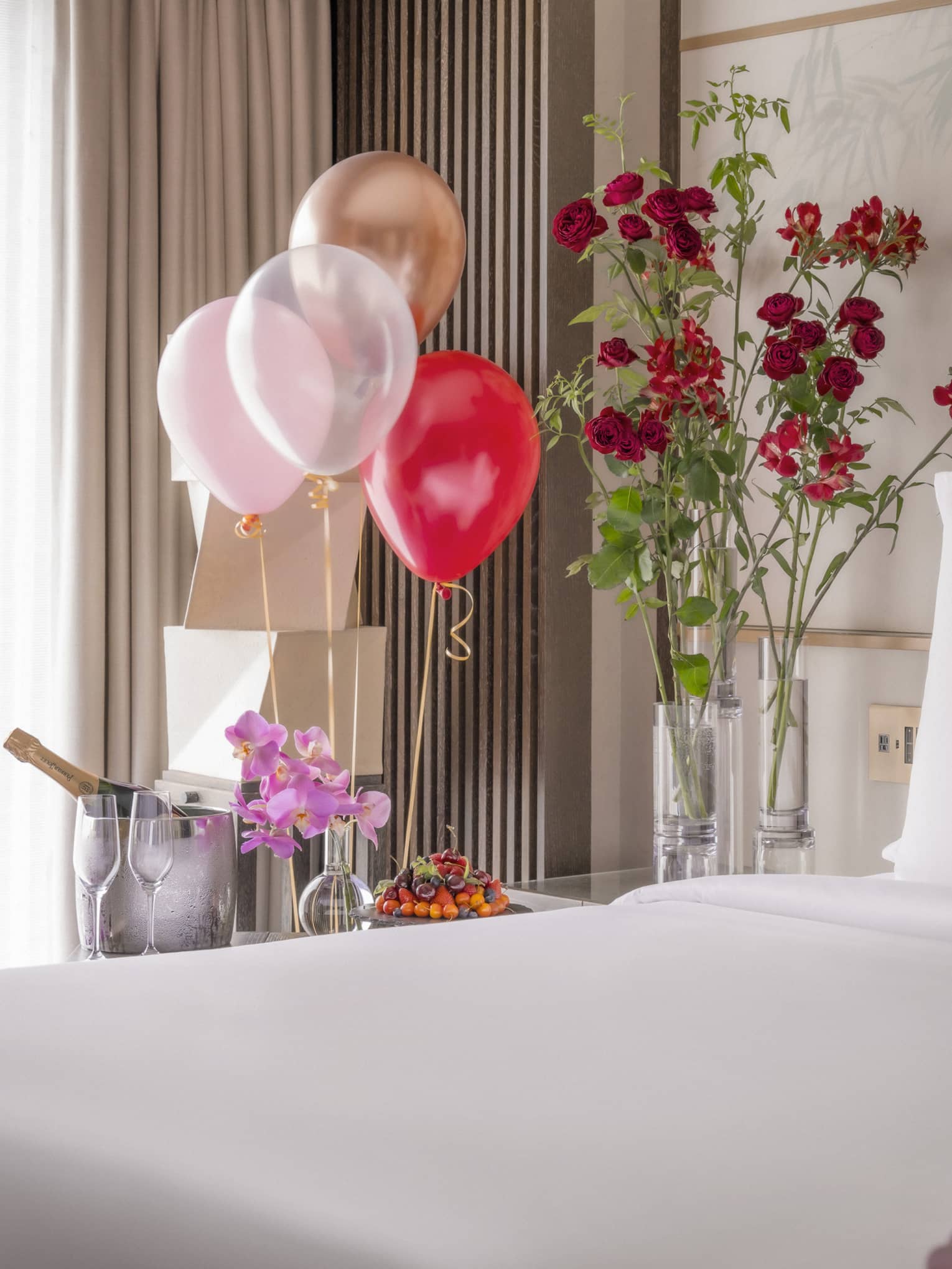 King bed with white linens surrounded by colourful balloons and ice bucket of champagne nearby