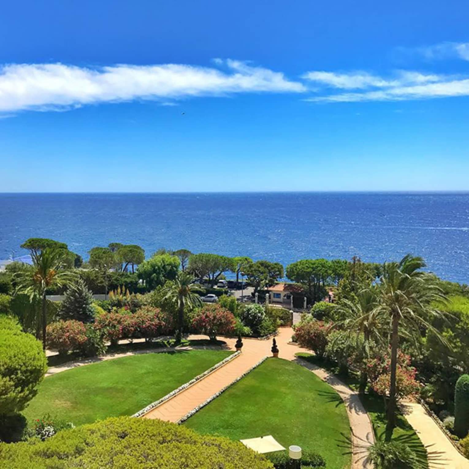 View across green lawn, trees and sea under blue sky