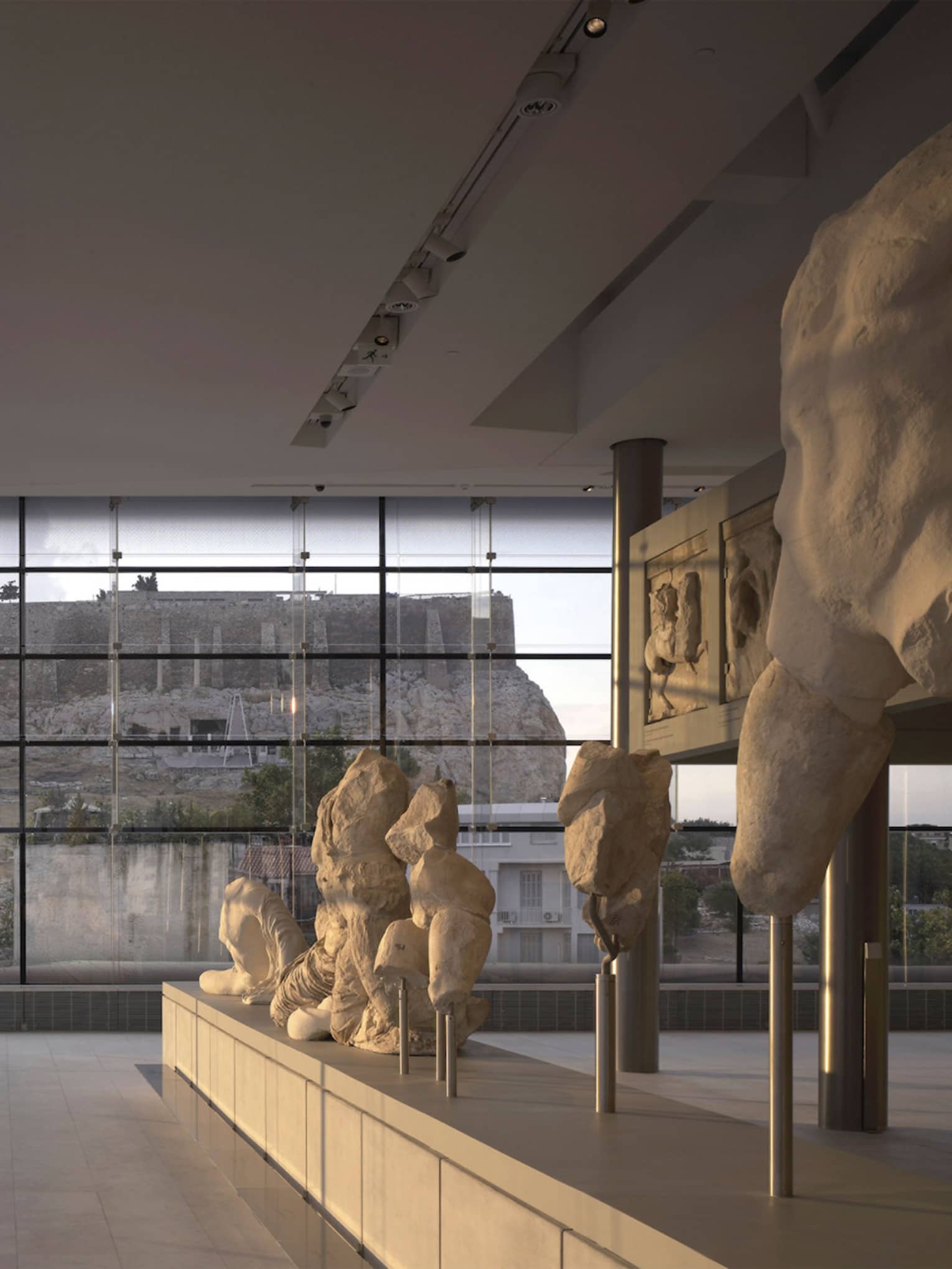 Greek sculptures on display in glass room overlooking ruins at Acropolis Museum