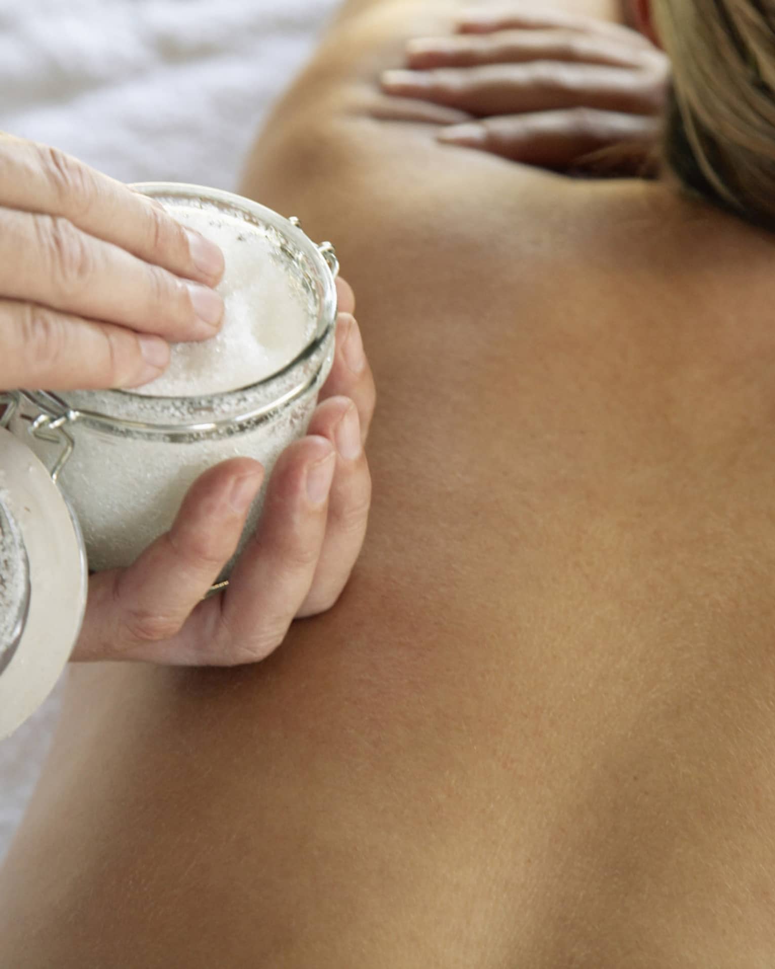 Jar of sea salt scrub above woman's bare back in spa
