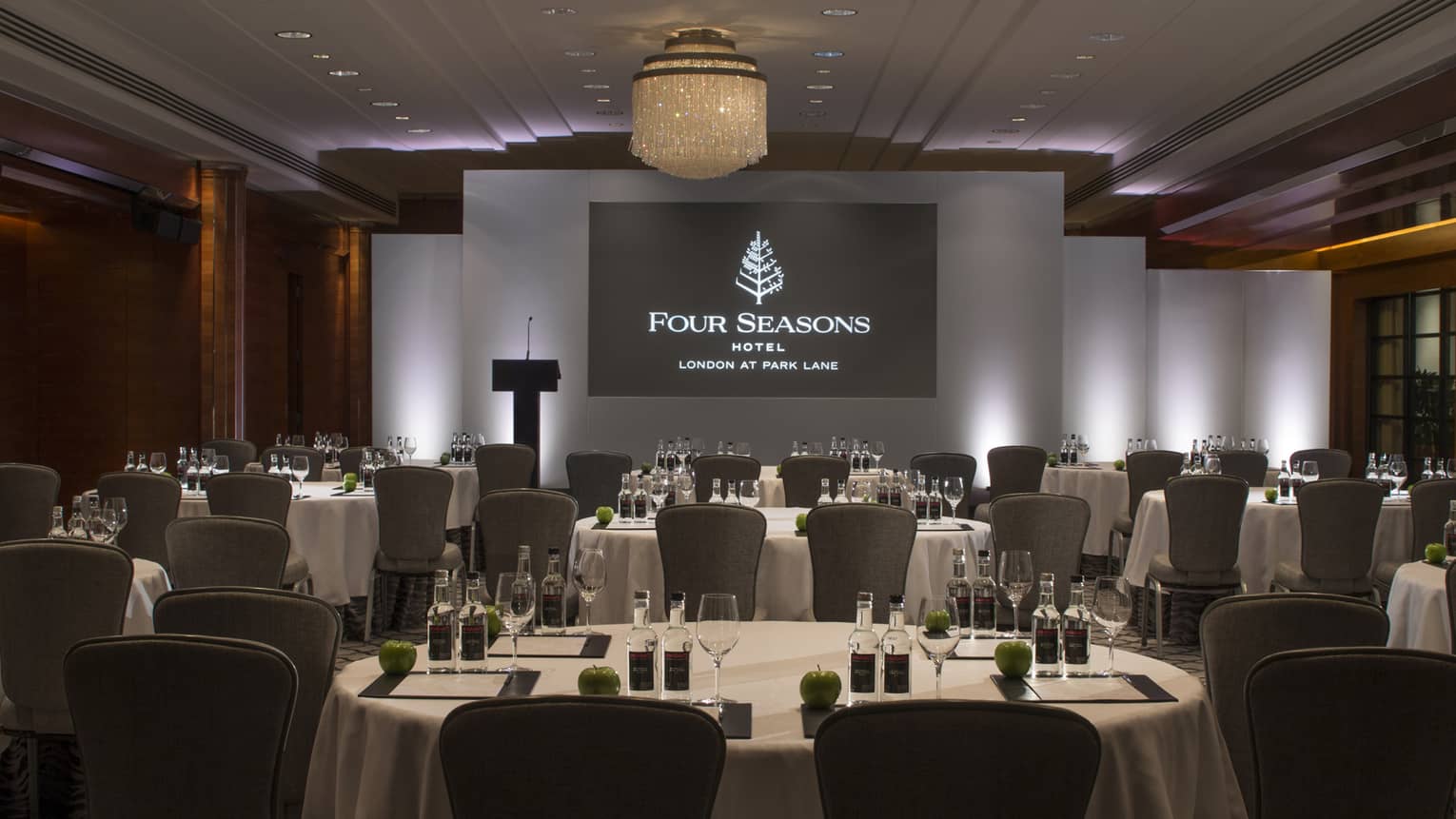 Round banquet tables by projector screen with Four Seasons Hotel London at Park Lane logo
