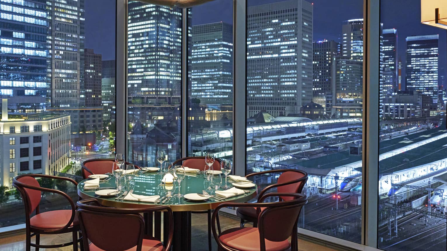 A round table and six chairs at Maison Marunouchi, floor-to-ceiling windows with views of downtown Tokyo at night