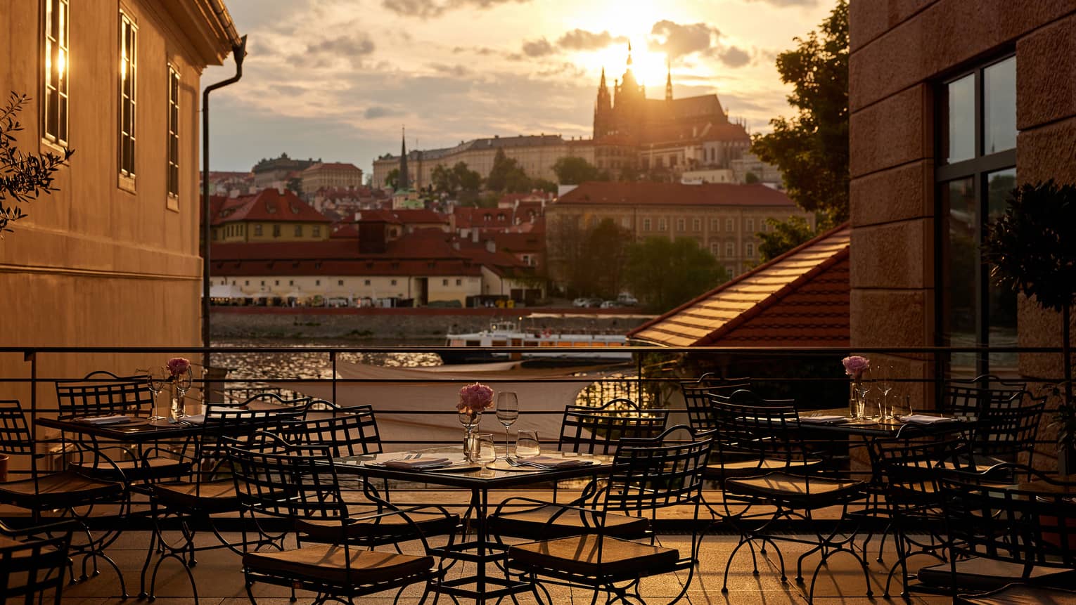 Restaurant terrace with black bistro dining tables with views of the Vltava River and Prague Castle at sunset
