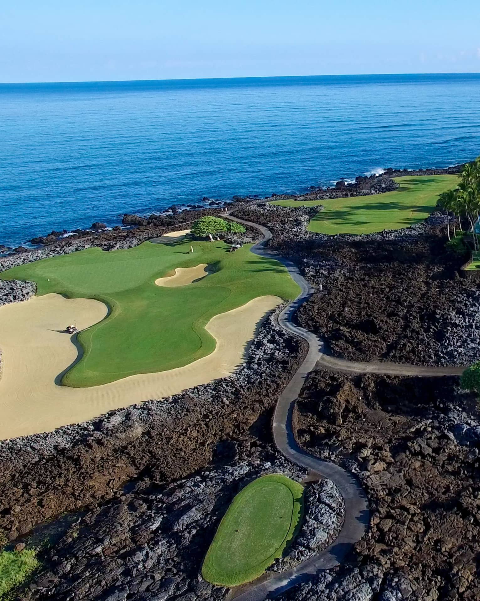 Aerial view of golf course greens in black volcanic rock on edge of ocean