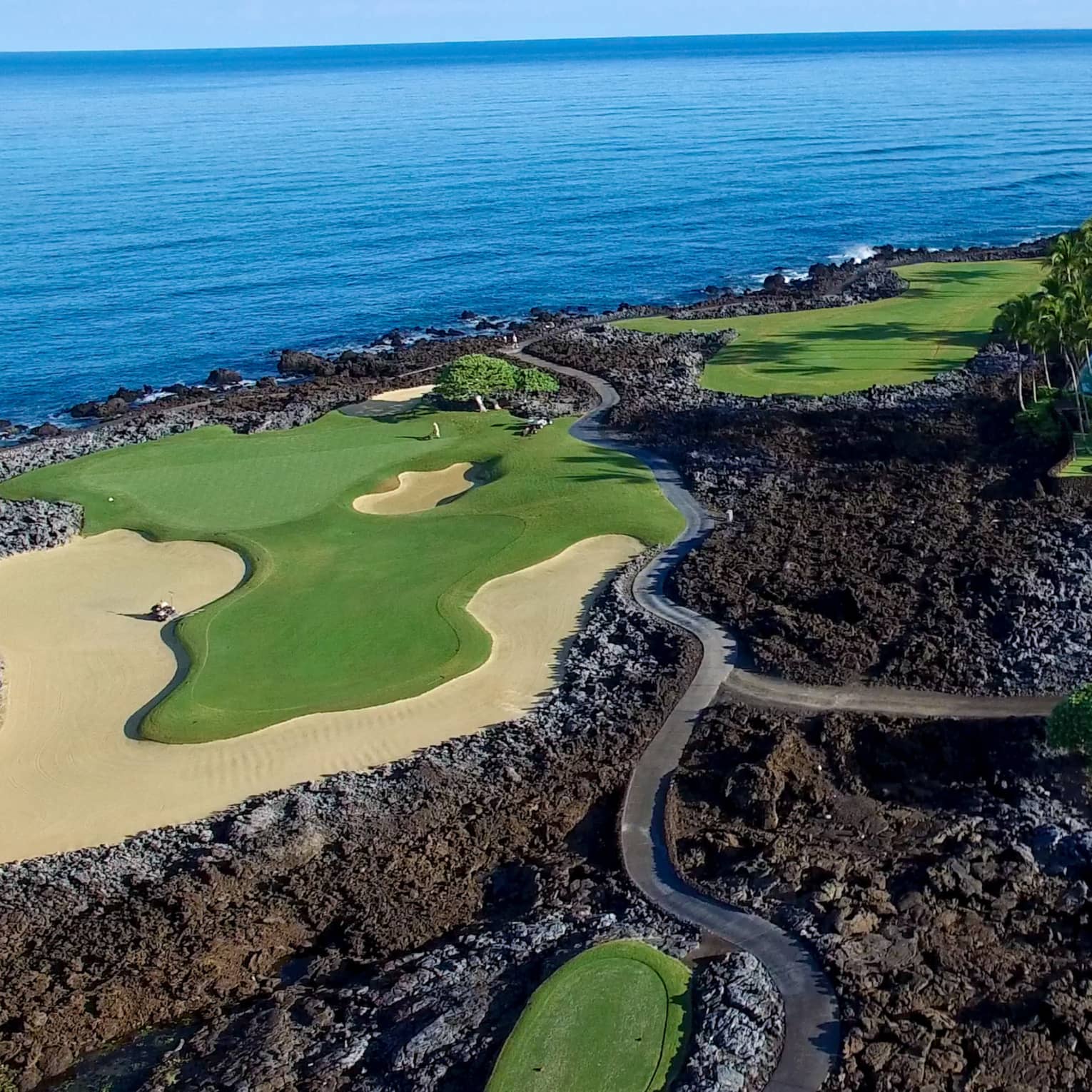 Aerial view of golf course greens in black volcanic rock on edge of ocean