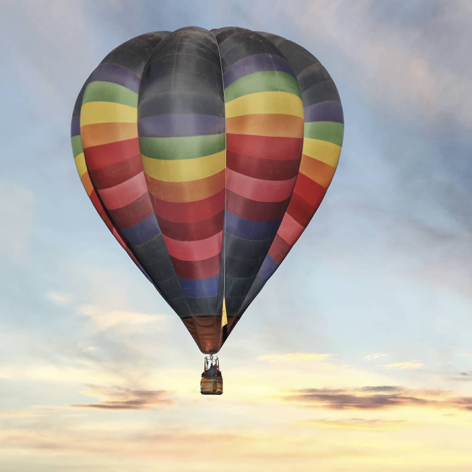 Rainbow-striped hot air balloon floats in the sky at sunset