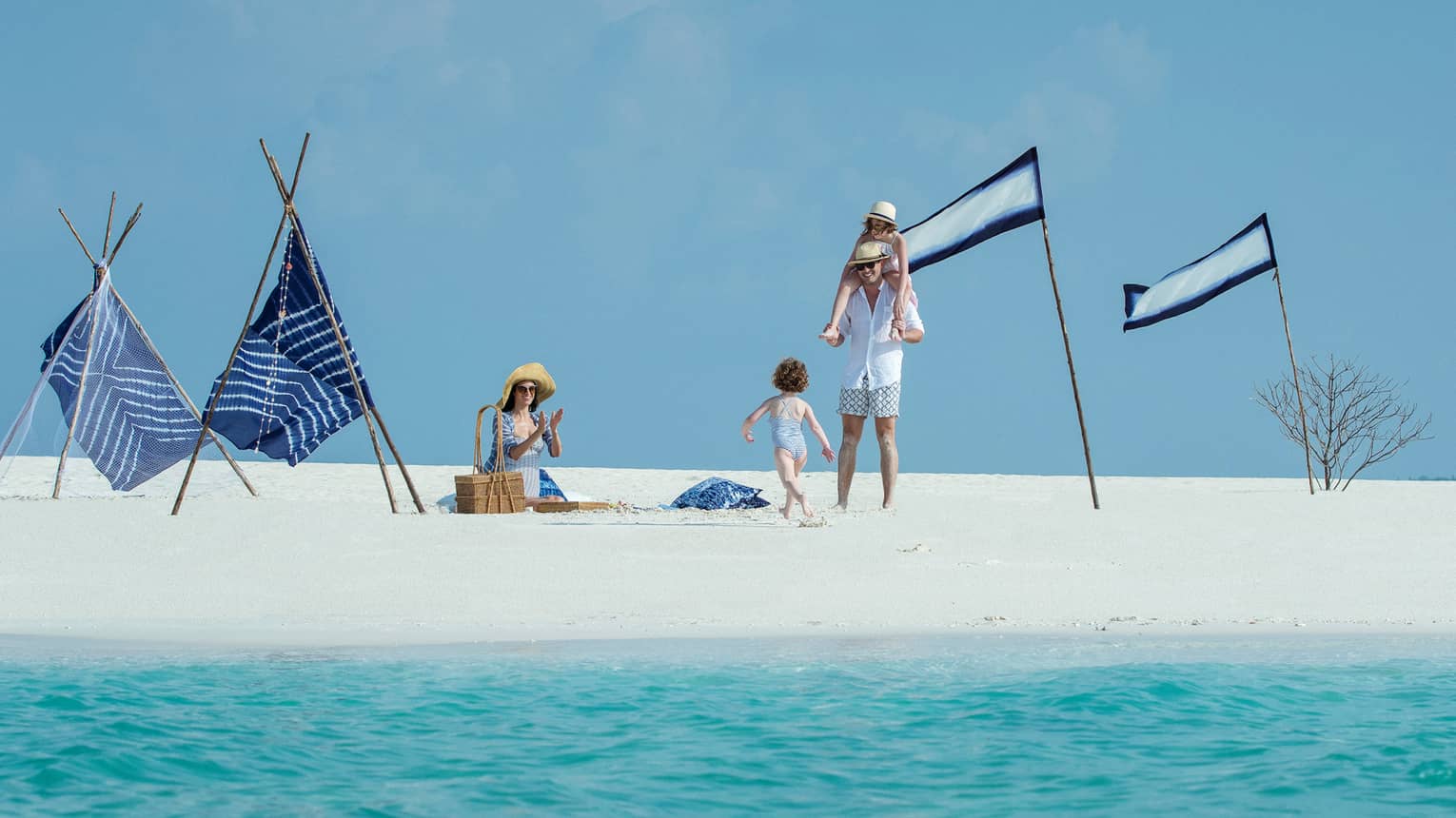 Family plays on white sand beach near blue flags, turquoise water