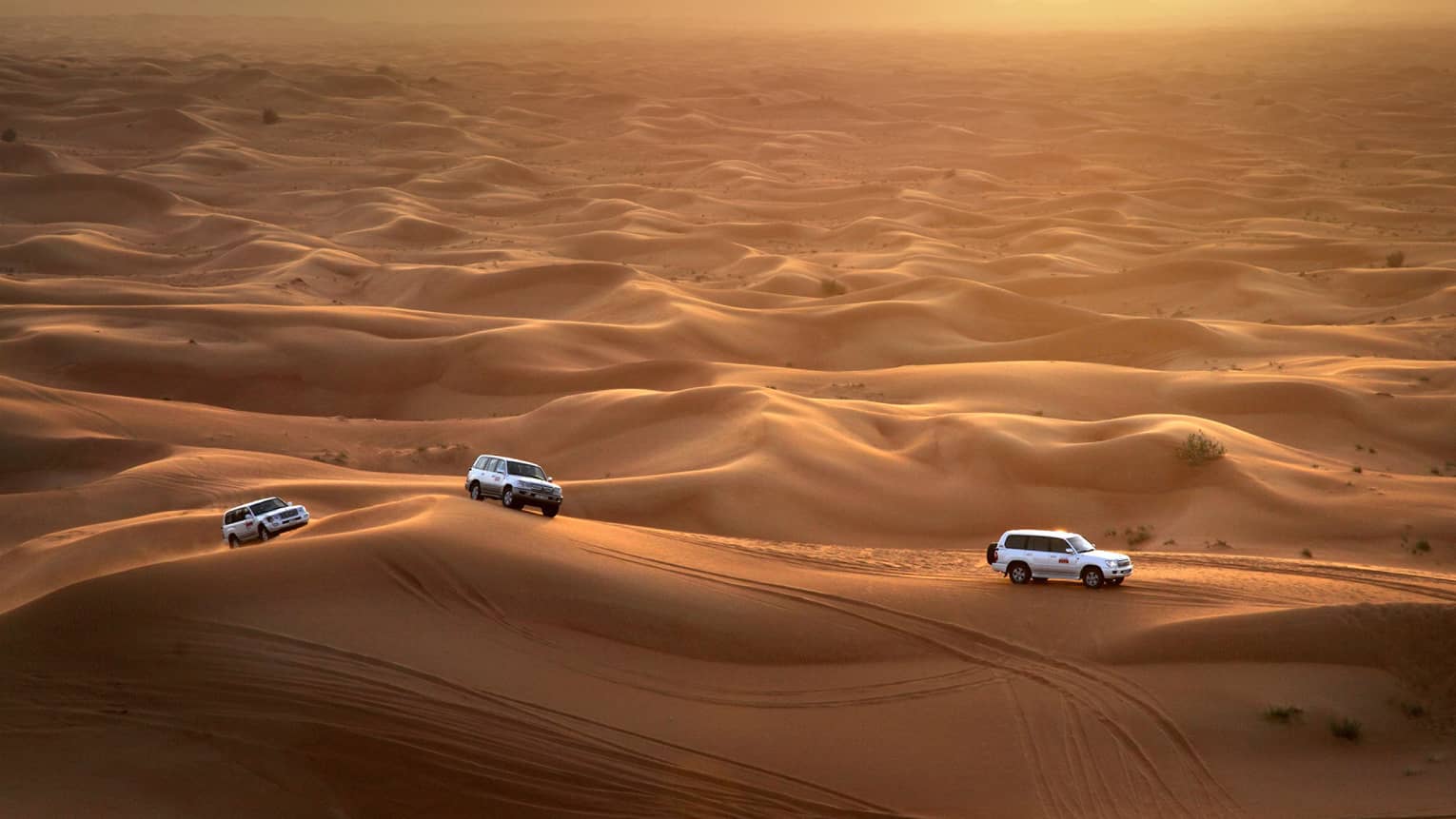 Aerial view of three Sundowner Desert Safari utility vehicles driving over sand dunes