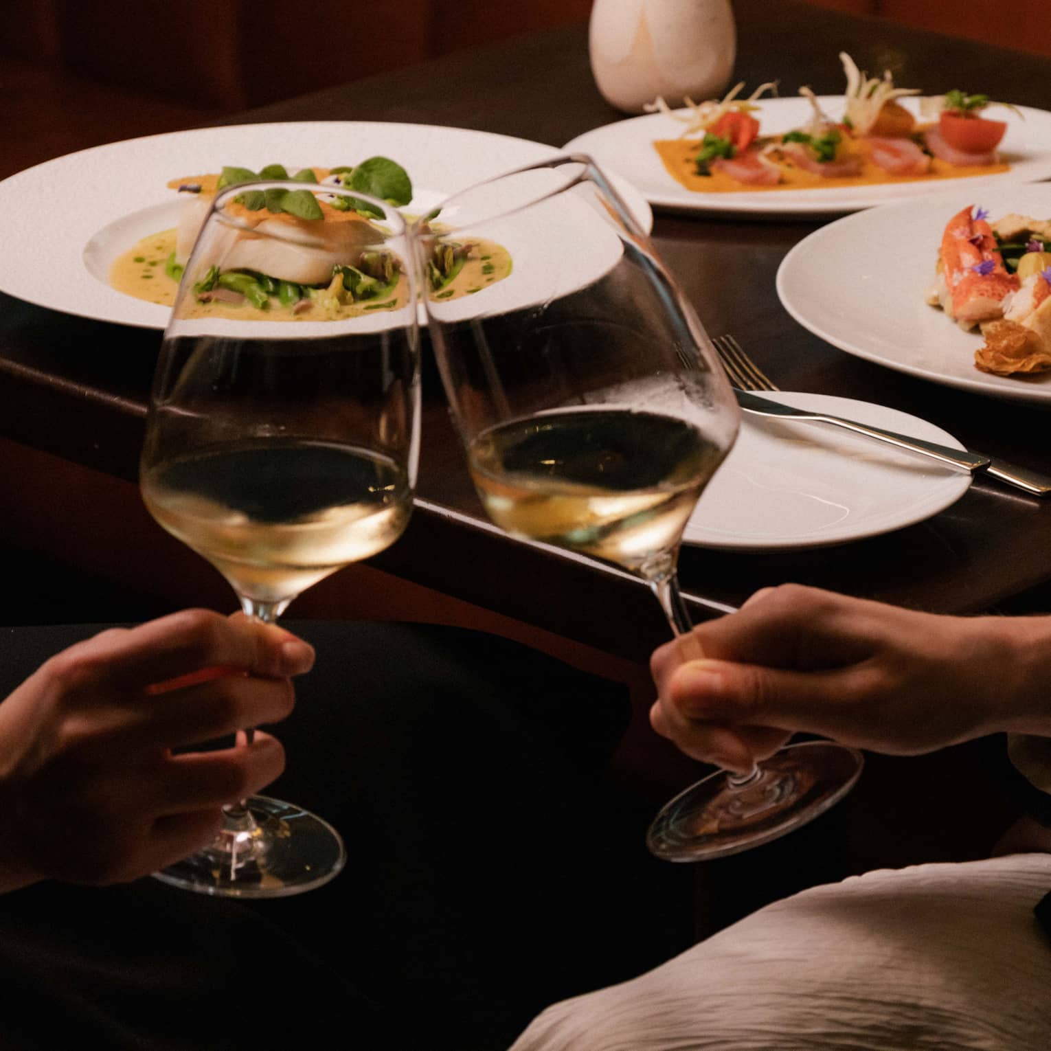Two people clink glasses of white wine at restaurant table