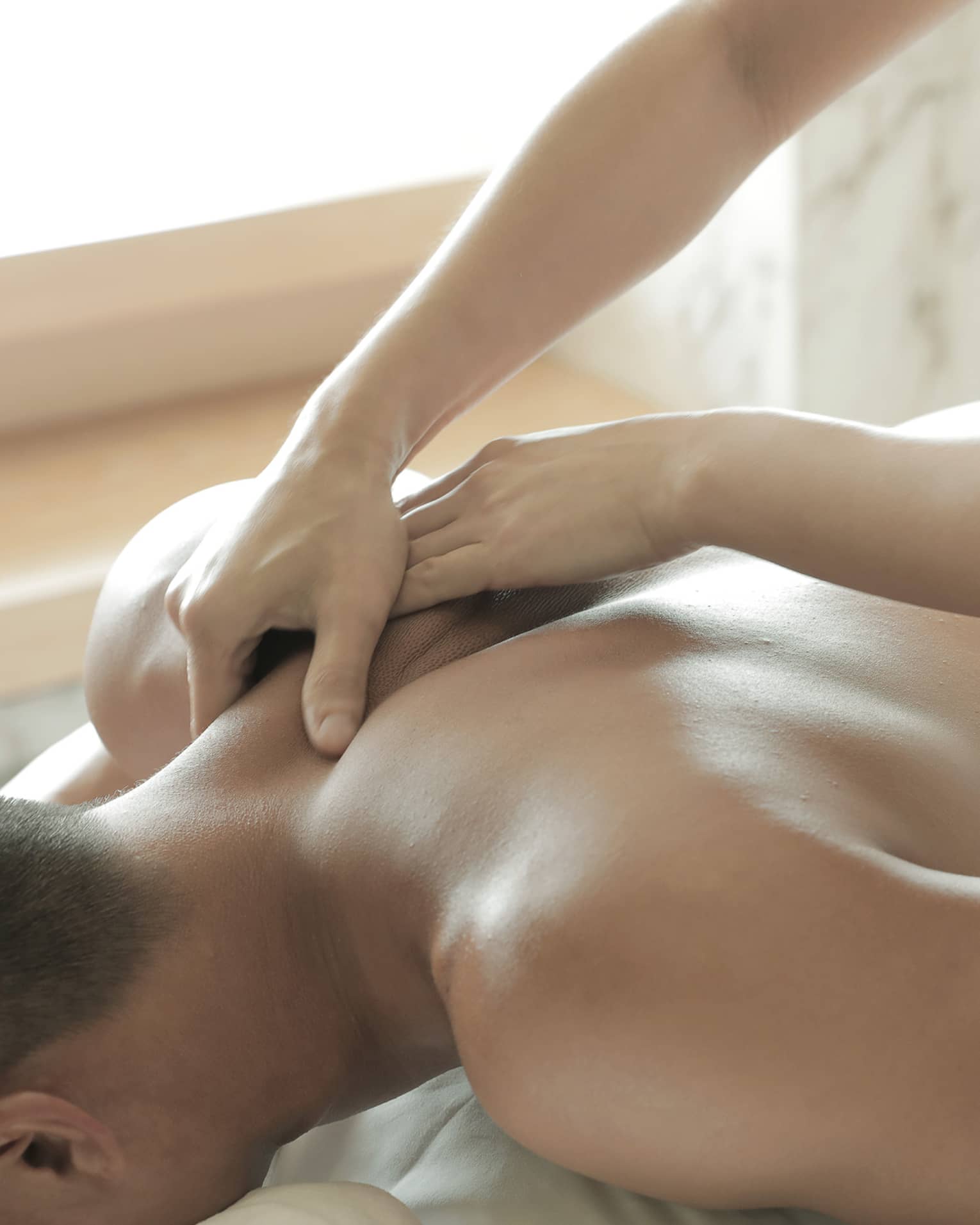 Spa masseuse massages man's bare back, shoulders