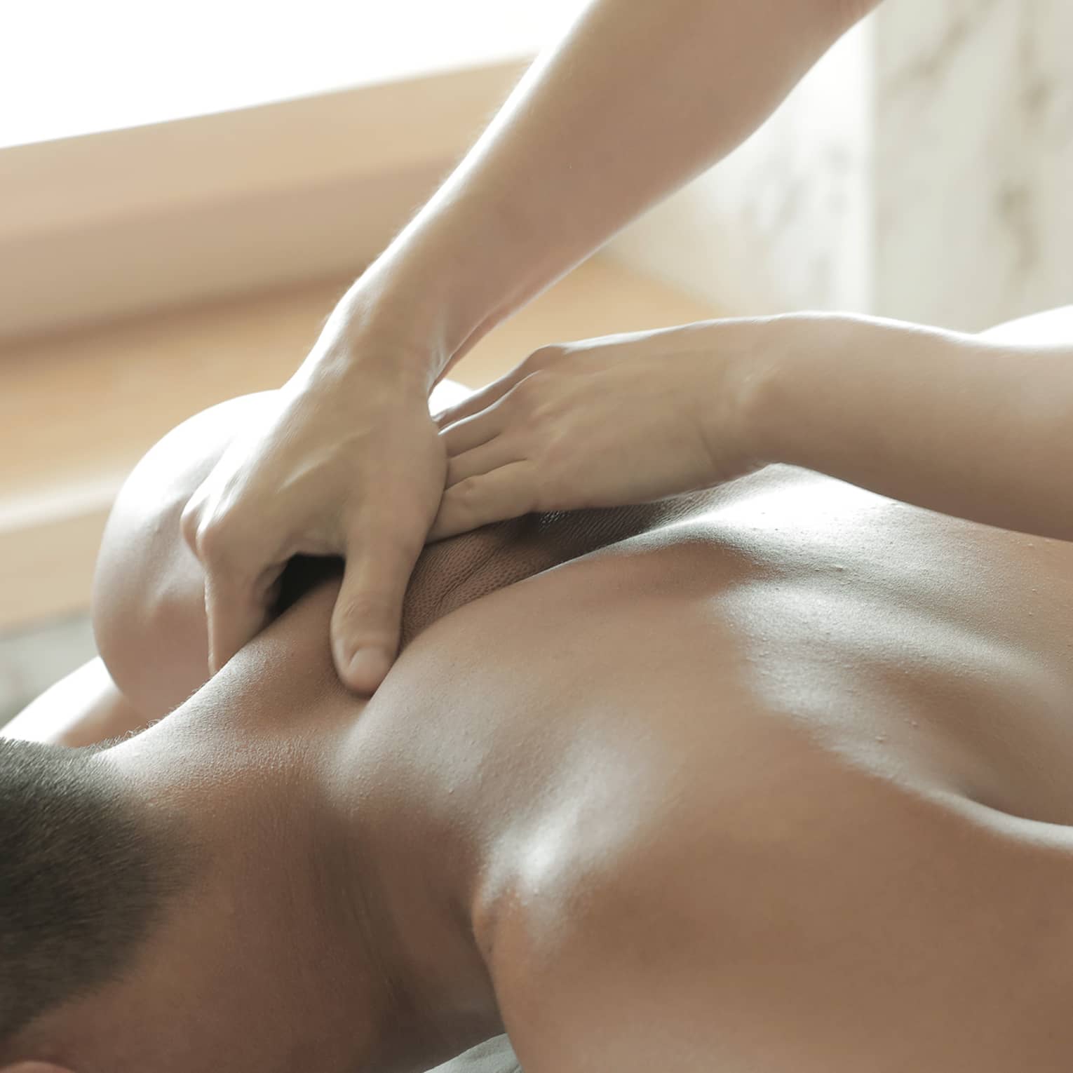 Spa masseuse massages man's bare back, shoulders