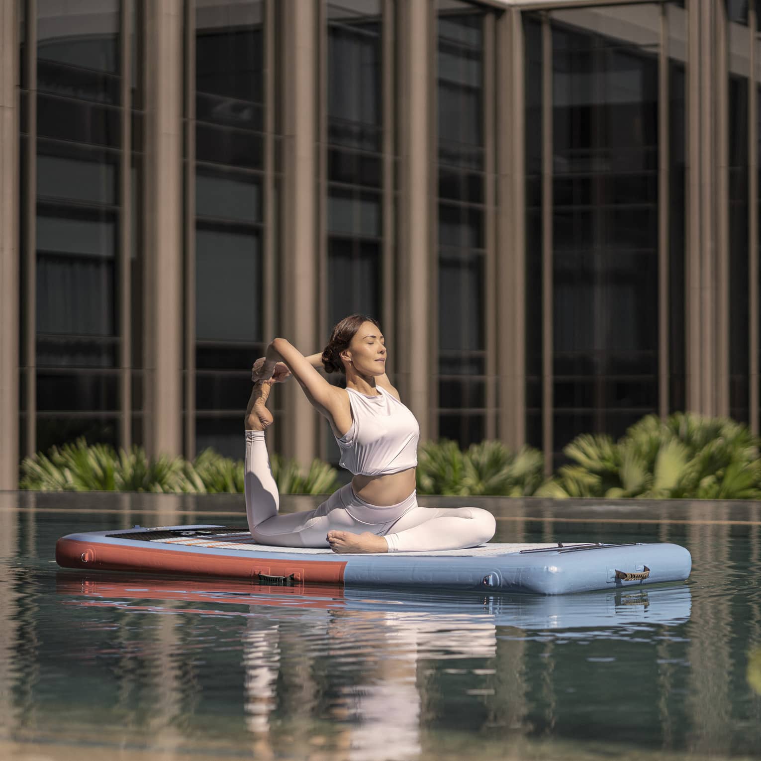 Woman doing a yoga pose on a floating paddle board in hotel pool