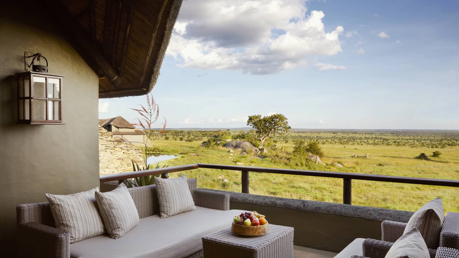 Villa terrace with beige wicker sofa and two chairs and expansive plains under blue skies
