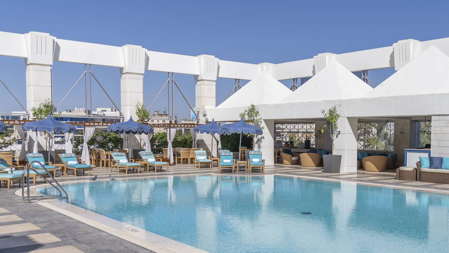 Outdoor pool surrounded by blue lounge chairs and four white tents