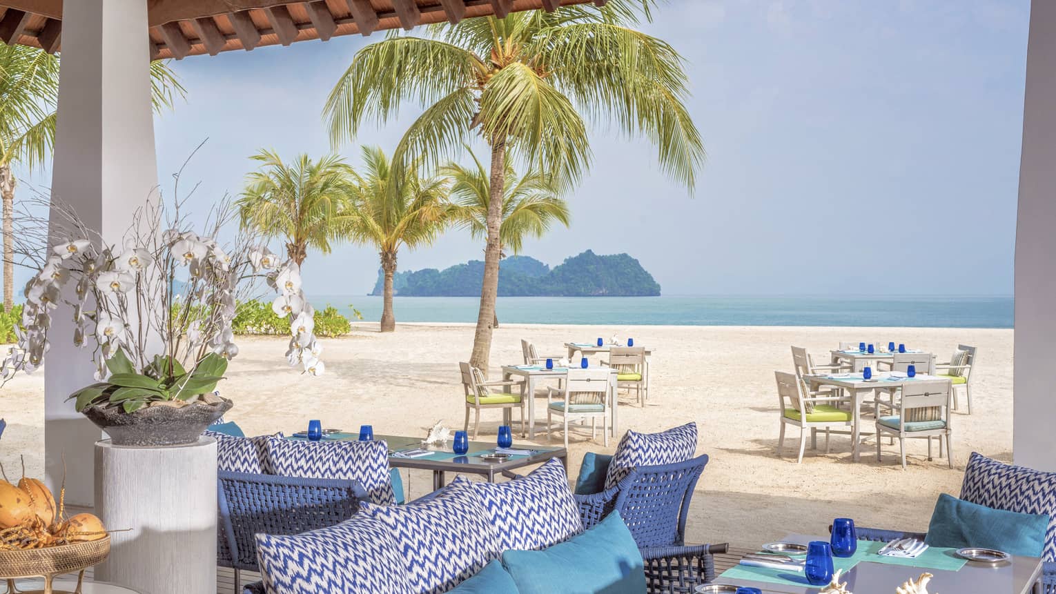 Terrace of ocean-view restaurant, blue cushions on sofa, turquoise place mats and blue glasses on table