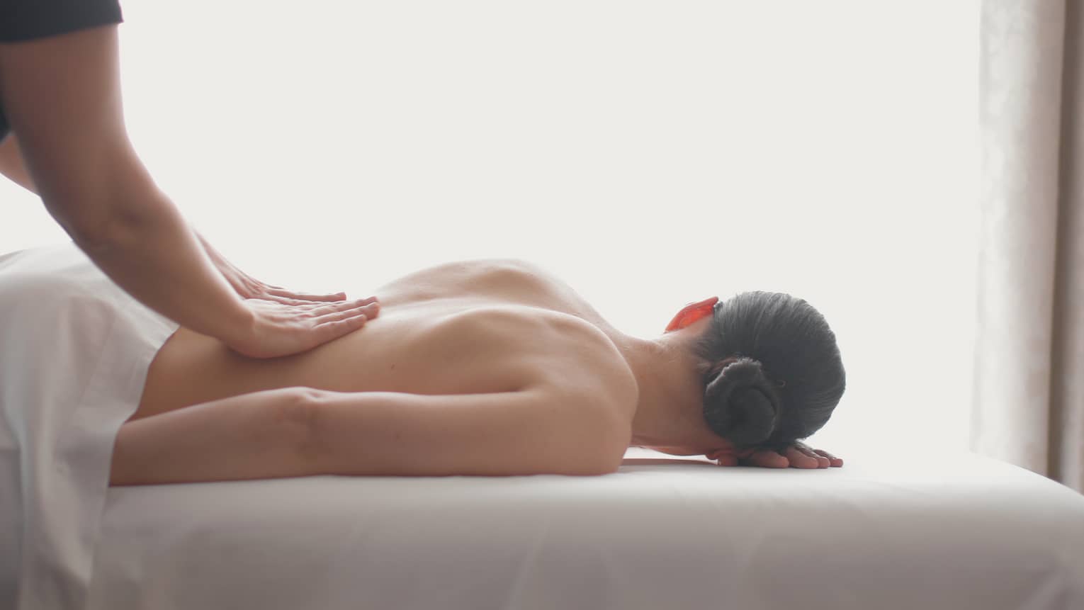 Side view of woman lying on massage table, hands massaging her bare shoulders