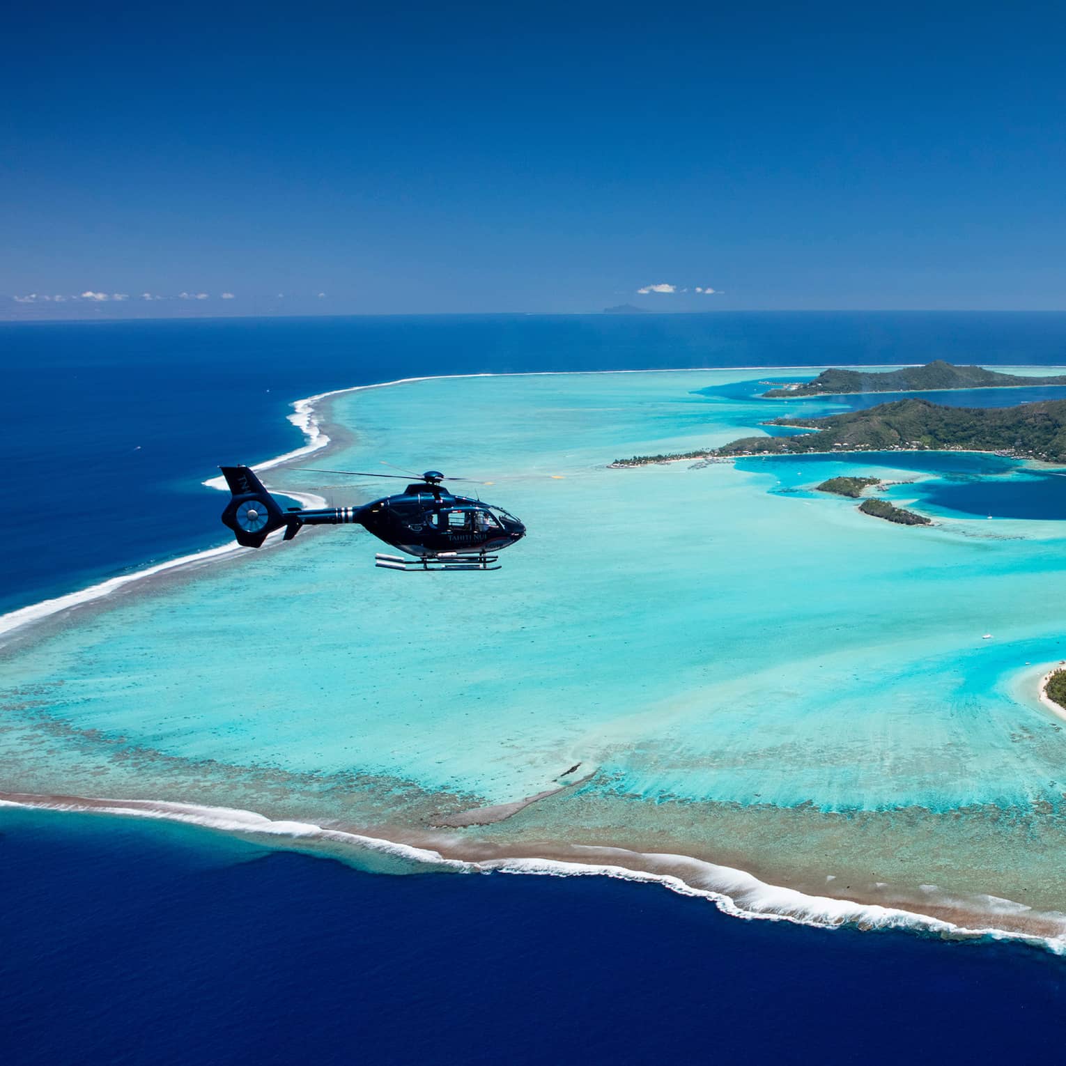 Aerial view of a helicopter flying over Bora Bora and the distinctive pastel blue lagoon that surrounds the islands.