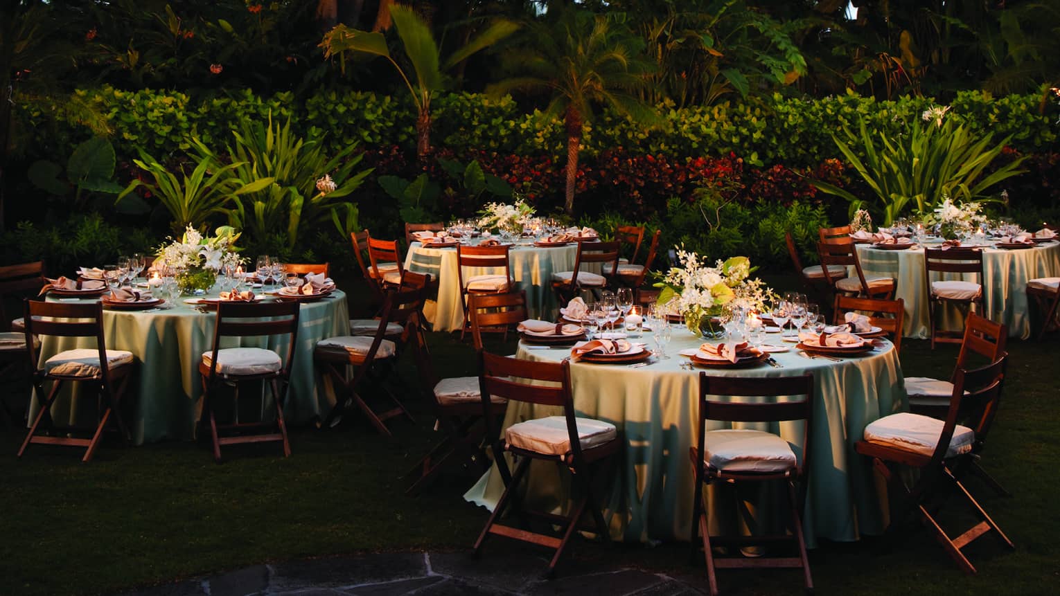 Pink paper lanterns hang from trees over banquet tables on Garden Lawn
