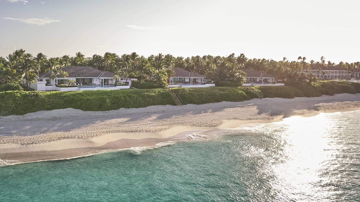 Sunlight over ocean, private sand beach and row of villas 