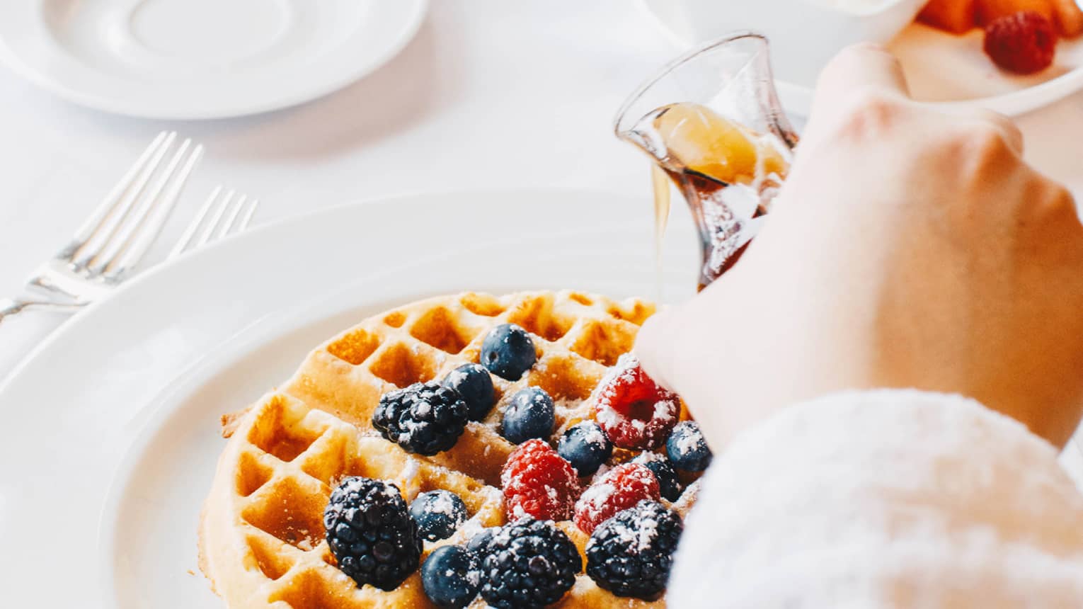 A guest pours syrup onto a Belgian waffle covered in berries