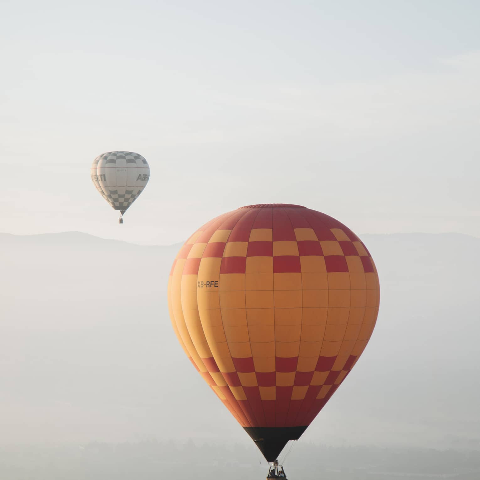 Yellow hot air balloon with red checkers in sky, hot air ballon in distance
